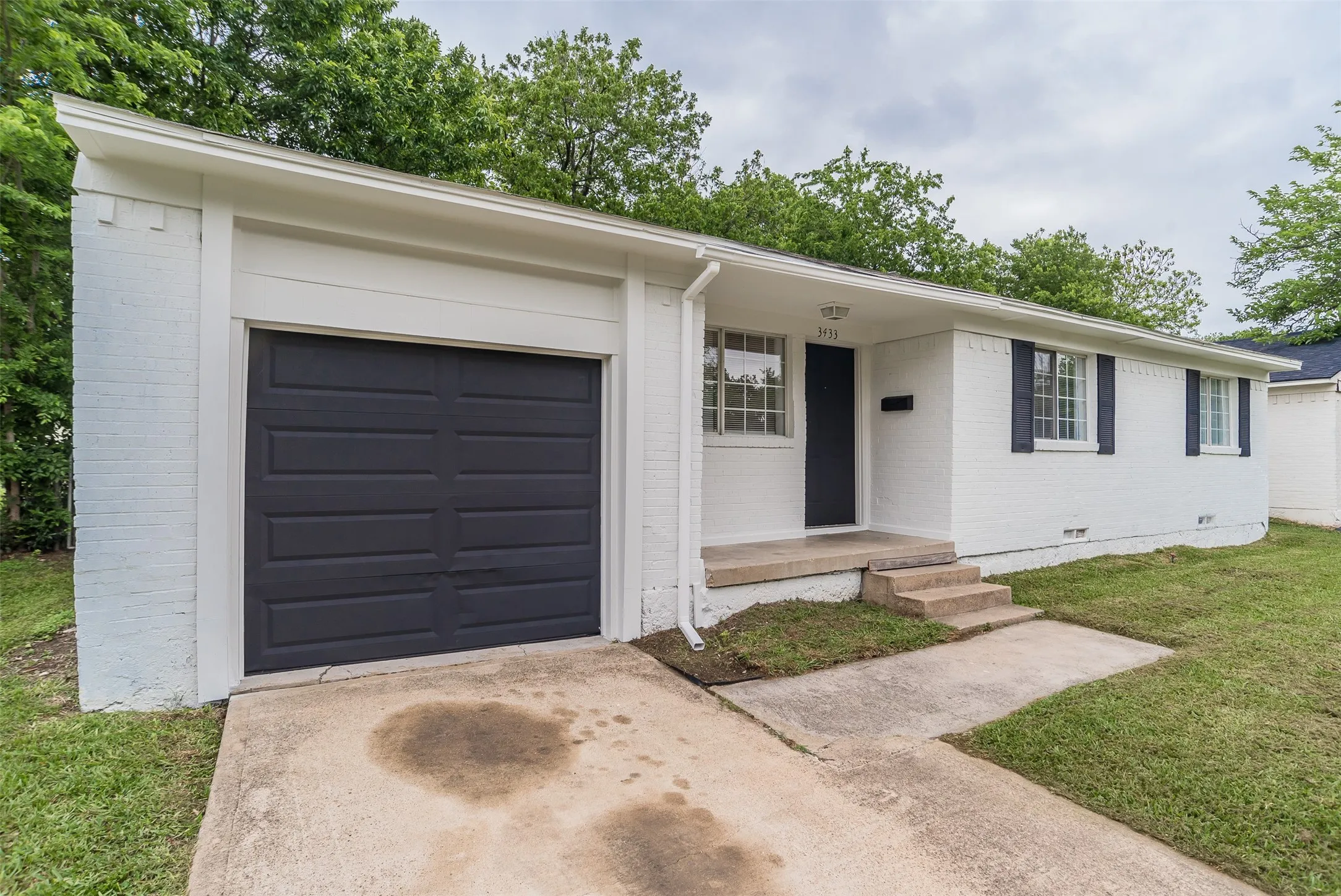 White brick exterior featuring a dark gray garage door, dark gray front door, and dark window shutters