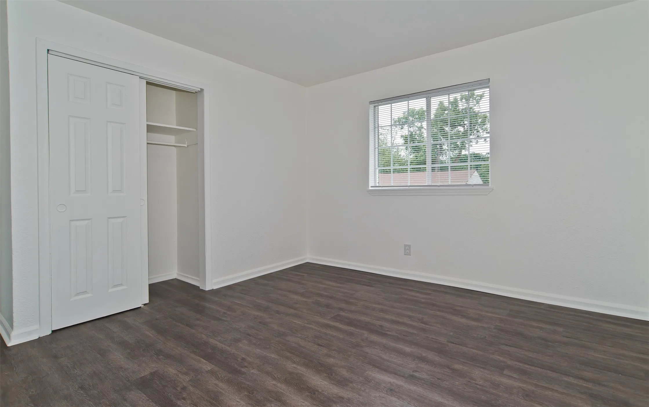 Spacious room featuring dark wood-finish flooring, white walls, and bright white trim