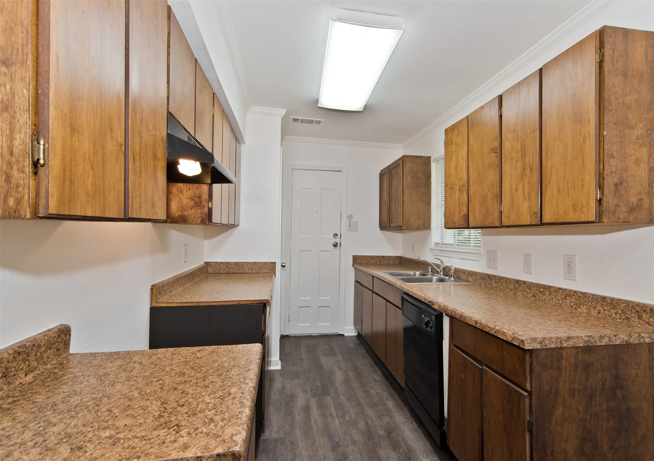Galley kitchen featuring wood cabinetry, speckled countertops, a double basin stainless steel sink, and wood-finish flooring