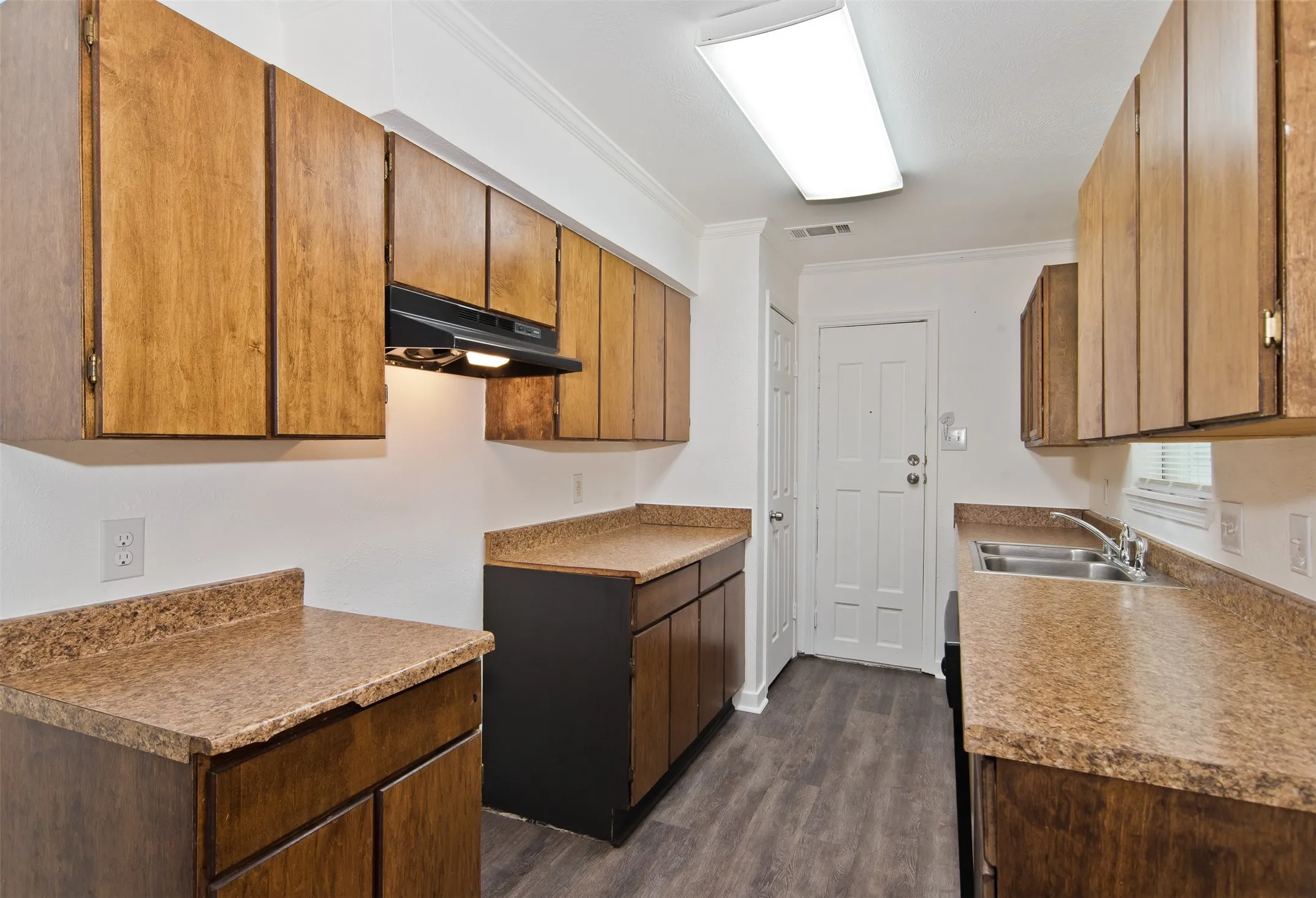 Kitchen featuring extensive cabinetry with wood finishes, ample counter space, a double basin stainless steel sink, a range hood with task lighting, and wood-finish​​‌​​​​‌​​‌‌​‌‌​​​‌‌​‌​‌​‌​​​‌​​ flooring