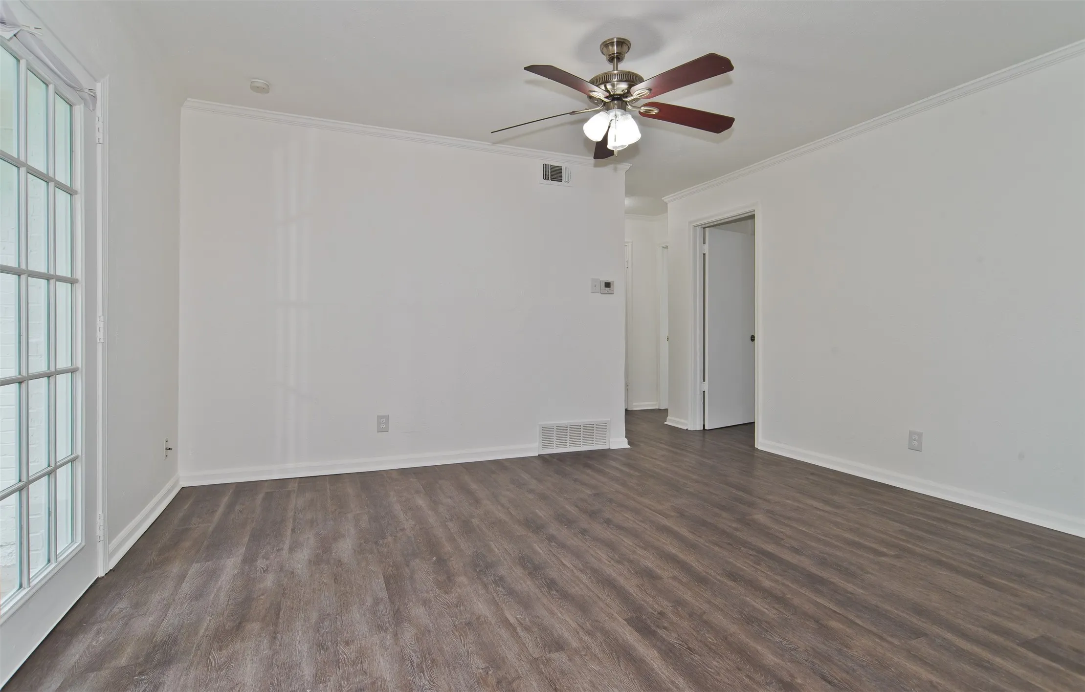 Spacious interior featuring wood-finish flooring, white walls, and a ceiling fan with integrated lighting Dining room opening to back yard