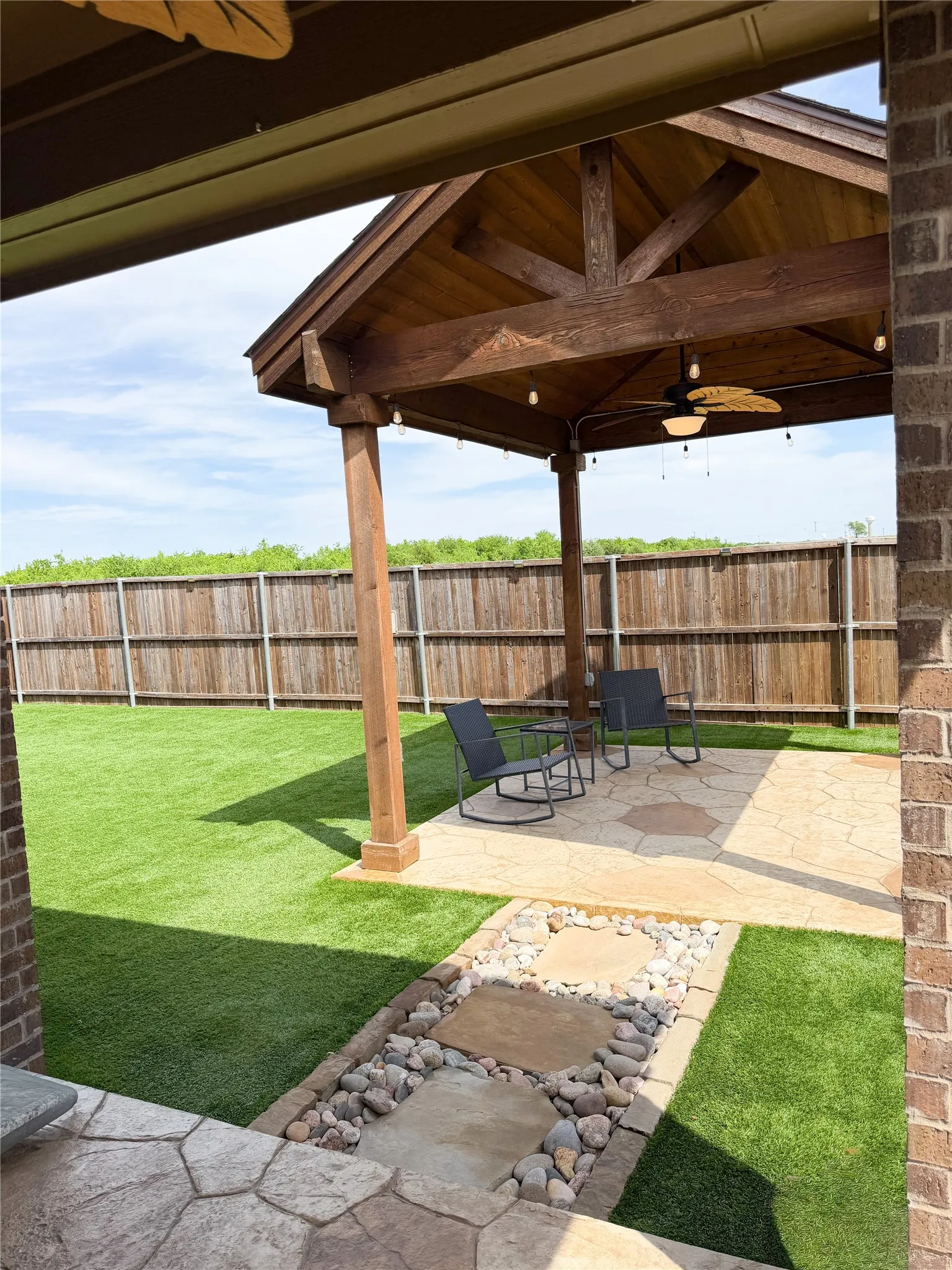 Step Outside to Enjoy Outdoor Living Space Flagstone and Rock Pathway Lead to 13 x 11 Artfully Crafted Pergola with a Solid Gabled Roof, Integrated Ceiling Fan, Bistro Lighting and Flagstone Inspired Stained Concrete. The Perfect Boutique Space for Year-Round Chilling.