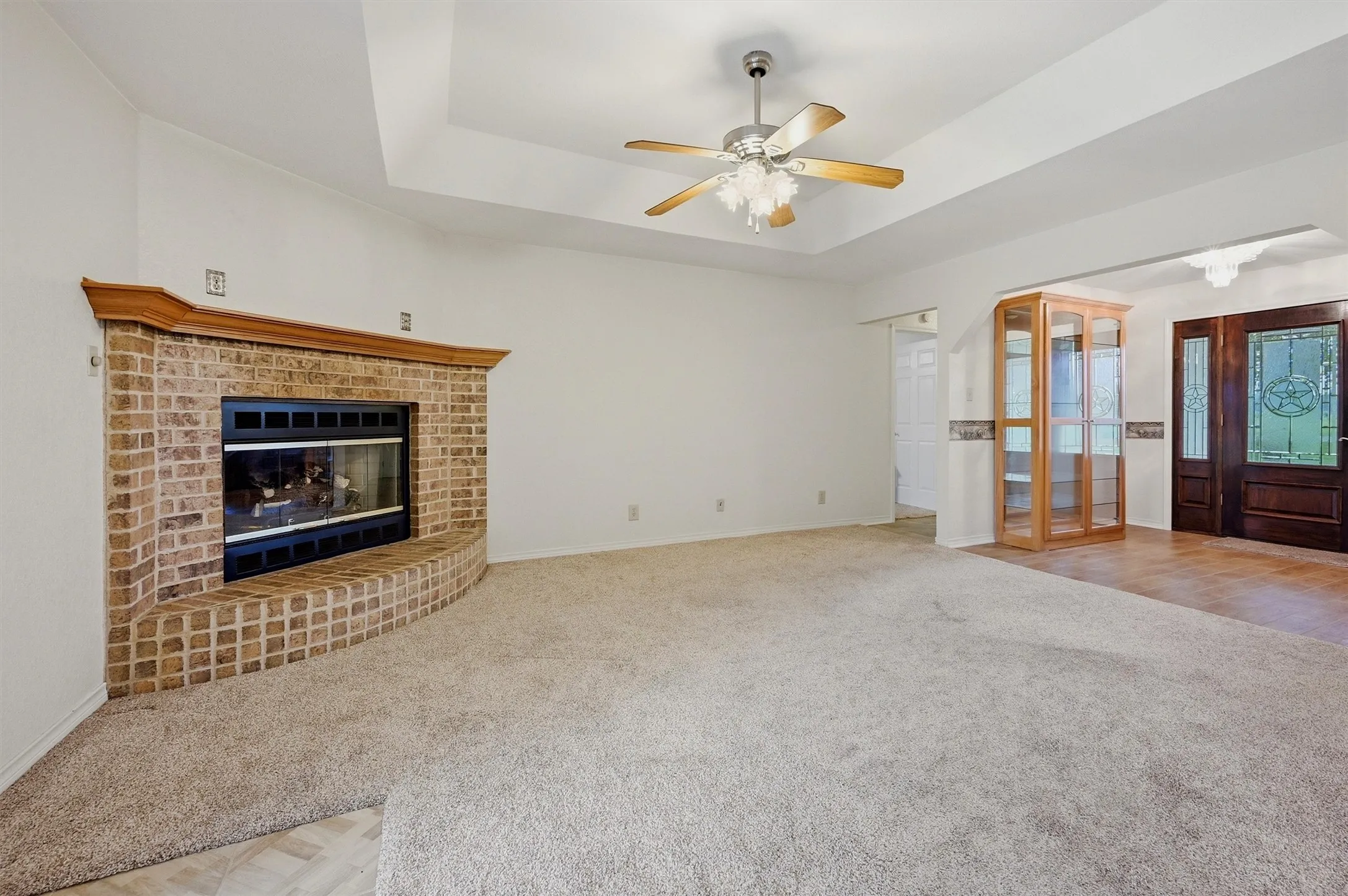 Spacious living area featuring a brick fireplace with a wood mantle, tray ceiling, and a ceiling fan