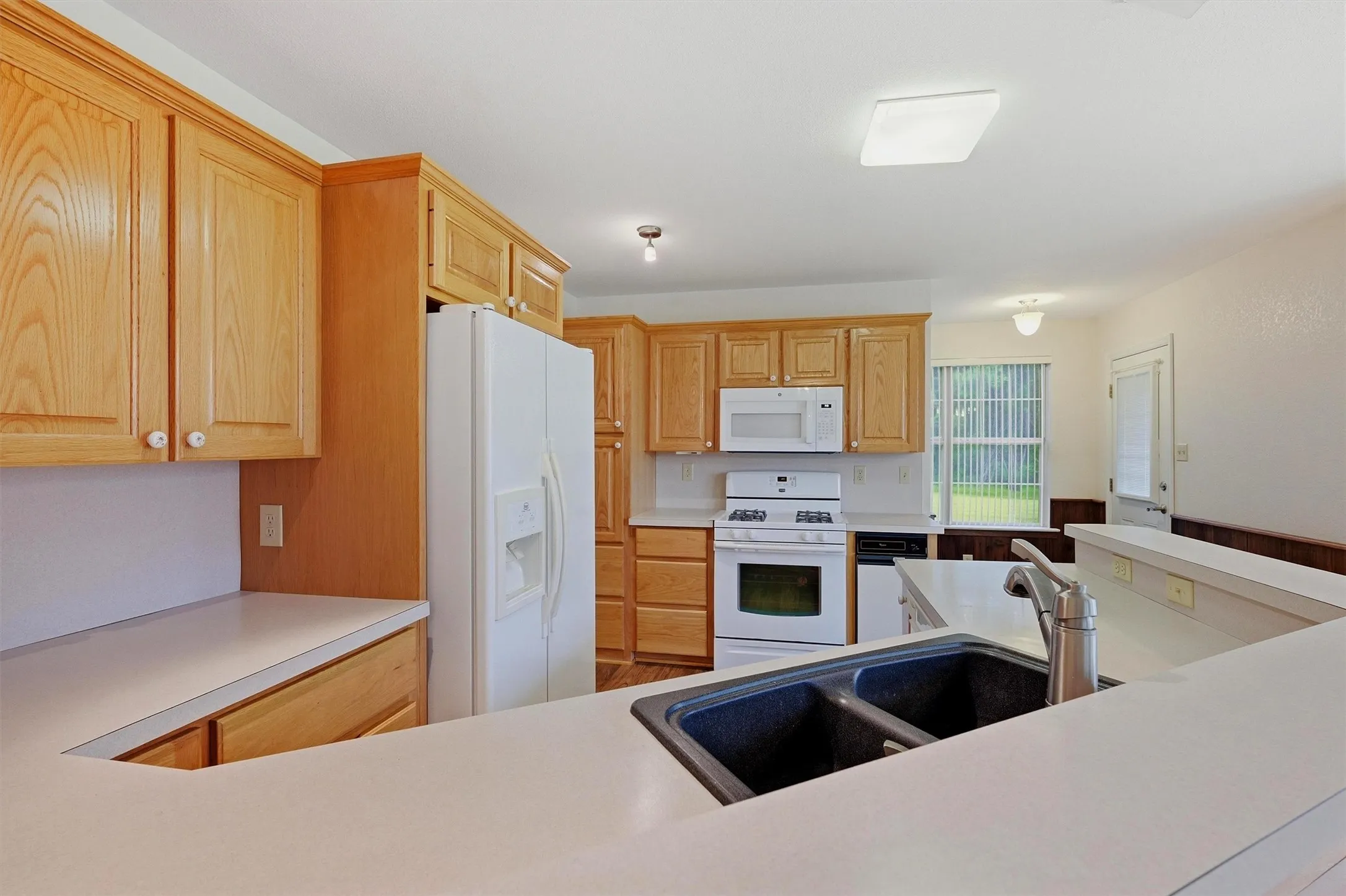 Kitchen featuring light-tone wood cabinetry, white countertops, and a dual-basin sink with a gooseneck faucet