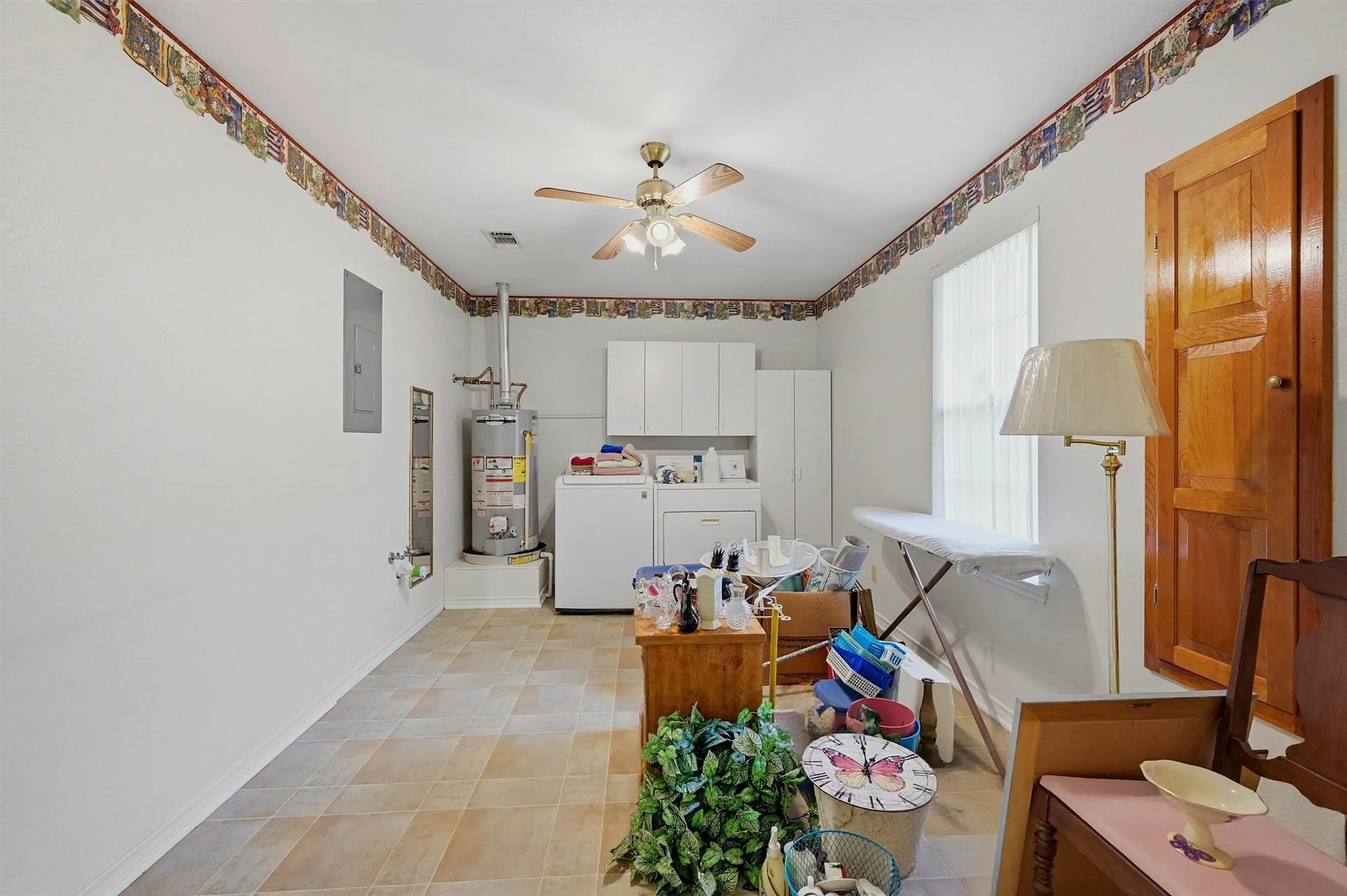 Utility room featuring a ceiling fan, window with vertical blinds, wall-mounted cabinetry, and tile flooring