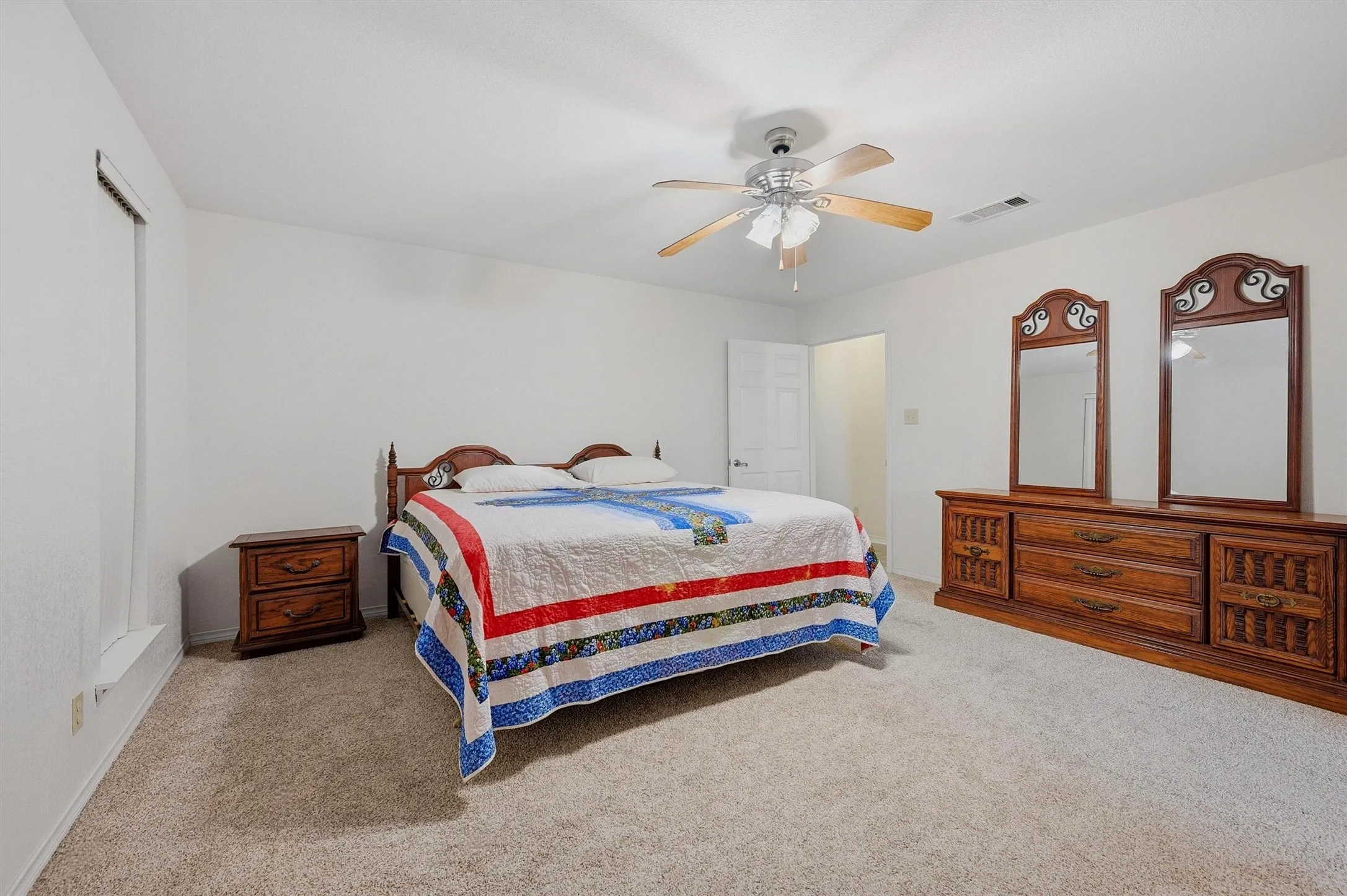 Spacious room featuring neutral carpeting, white walls, and a ceiling fan with light fixture