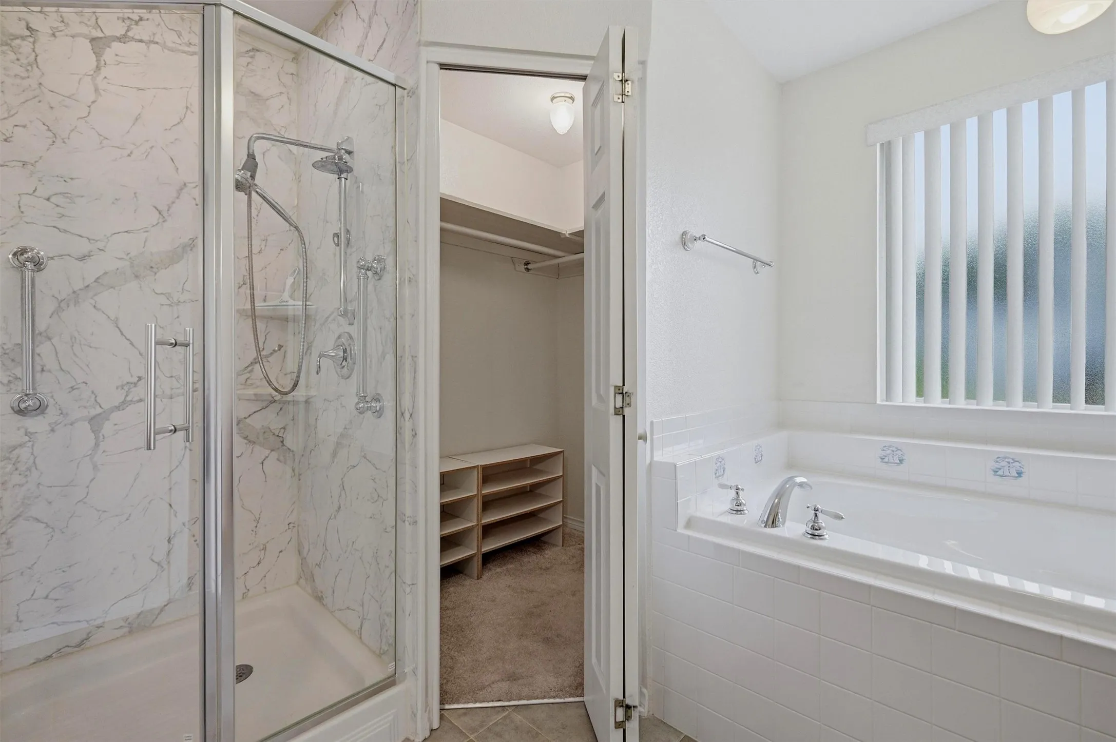 Glass-enclosed shower with a marble-patterned surround, an adjacent soaking tub with tiled surround, and a nearby walk-in closet featuring shelving and hanging space