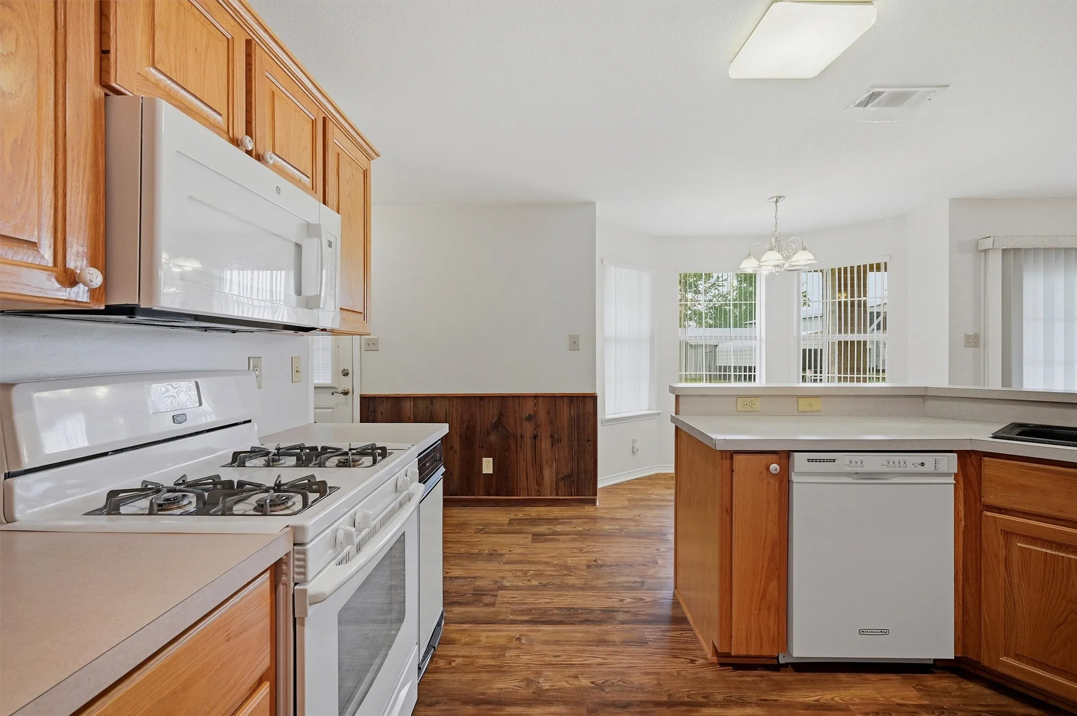 Kitchen featuring wood-finish flooring, wood cabinetry, white appliances, and a built-in dishwasher