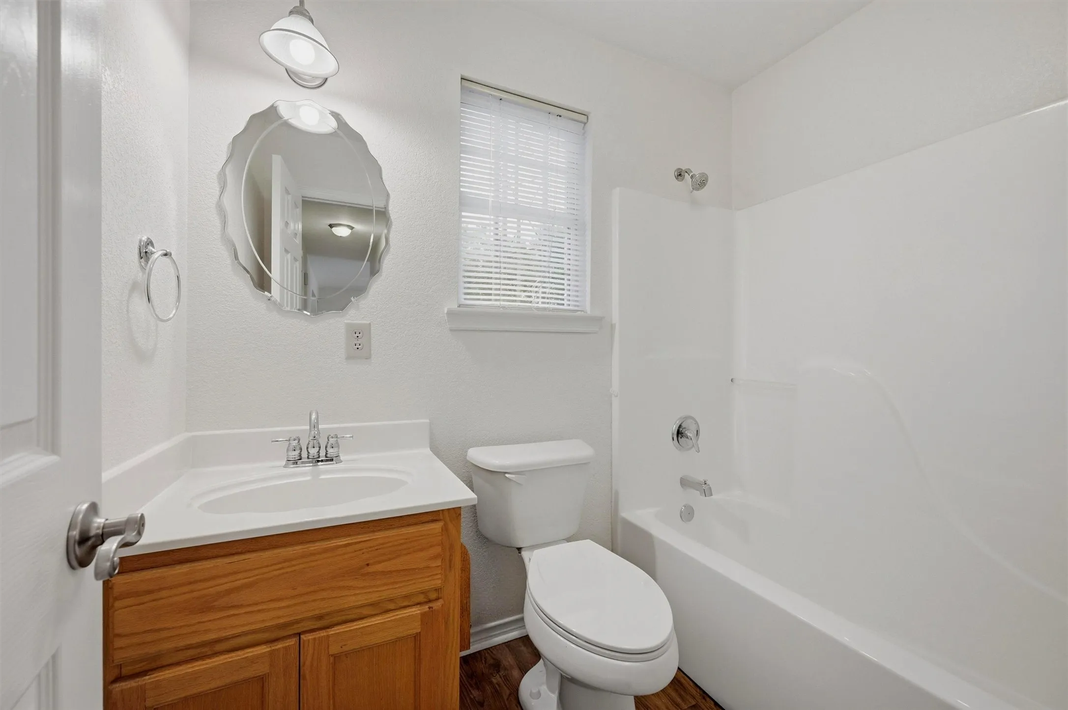 Bathroom featuring a wood-finish vanity with a white countertop and integrated sink, a scalloped mirror, a white toilet, and a white tub with shower