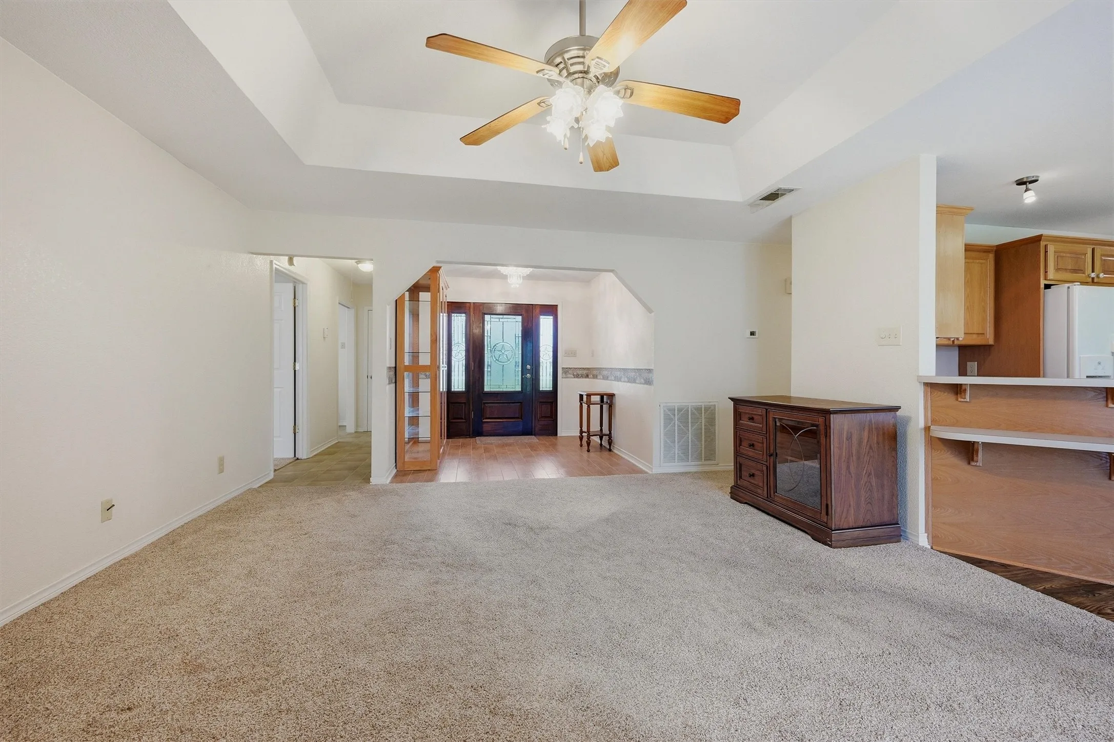 Carpeted living area featuring a tray ceiling with a ceiling fan, an arched entryway, and an adjacent wood-finish breakfast bar