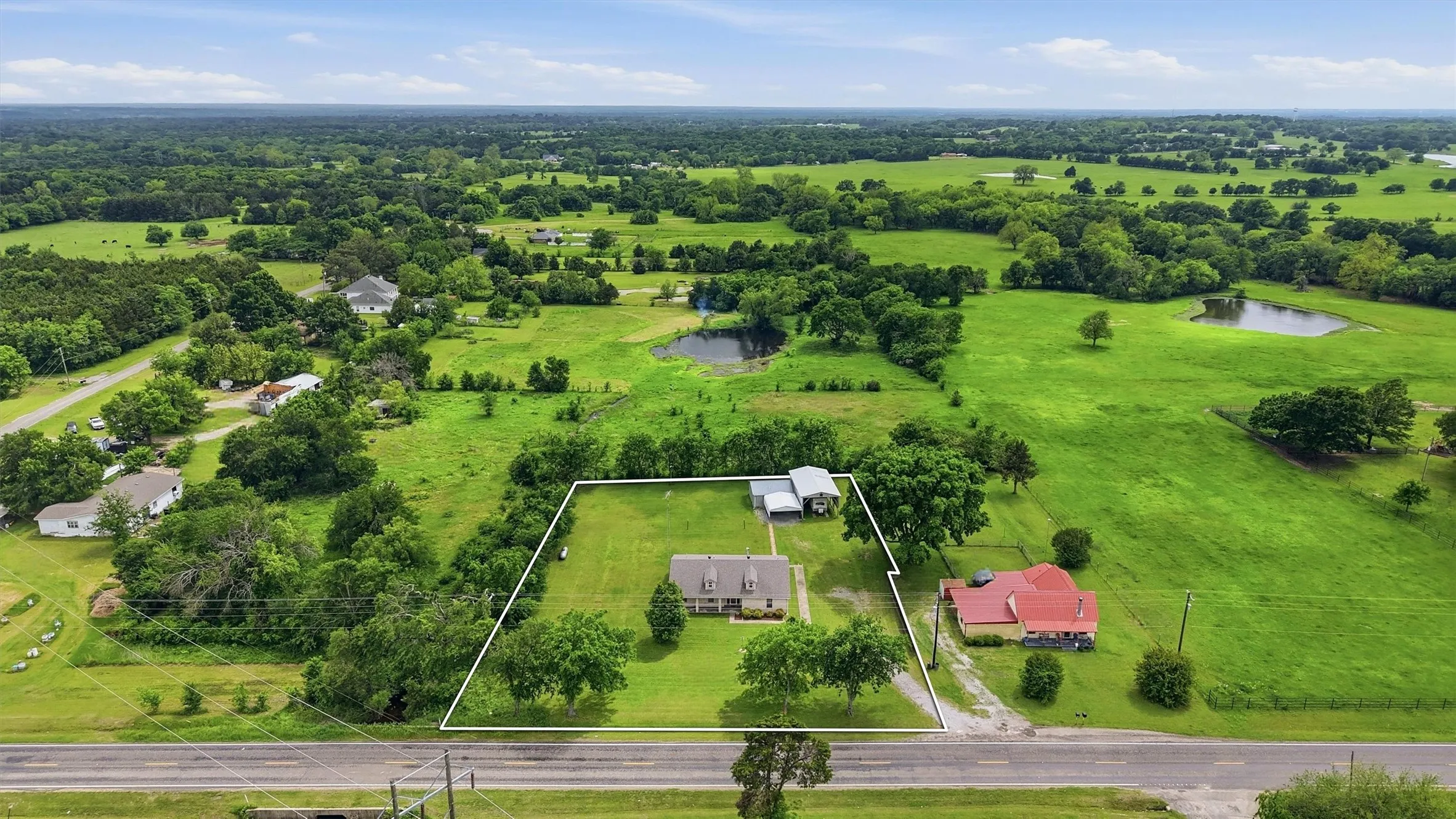 Aerial view showcasing a property with a light-colored main residence, an additional auxiliary structure, and a perimeter outlining the property boundaries