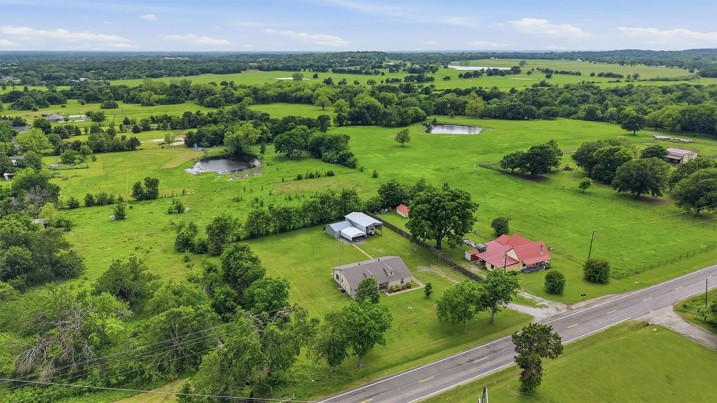 Expansive property featuring verdant fields, multiple ponds, mature trees, and direct road frontage