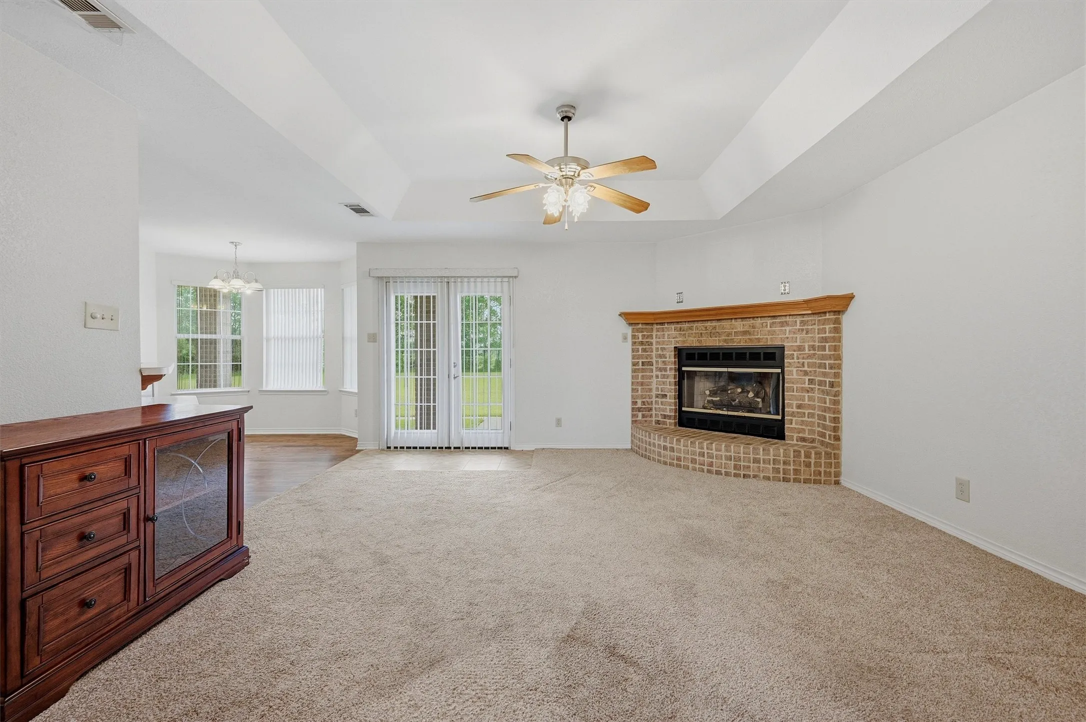 Spacious living area featuring a corner brick fireplace with a wood mantel, tray ceiling, and a ceiling fan with integrated lighting