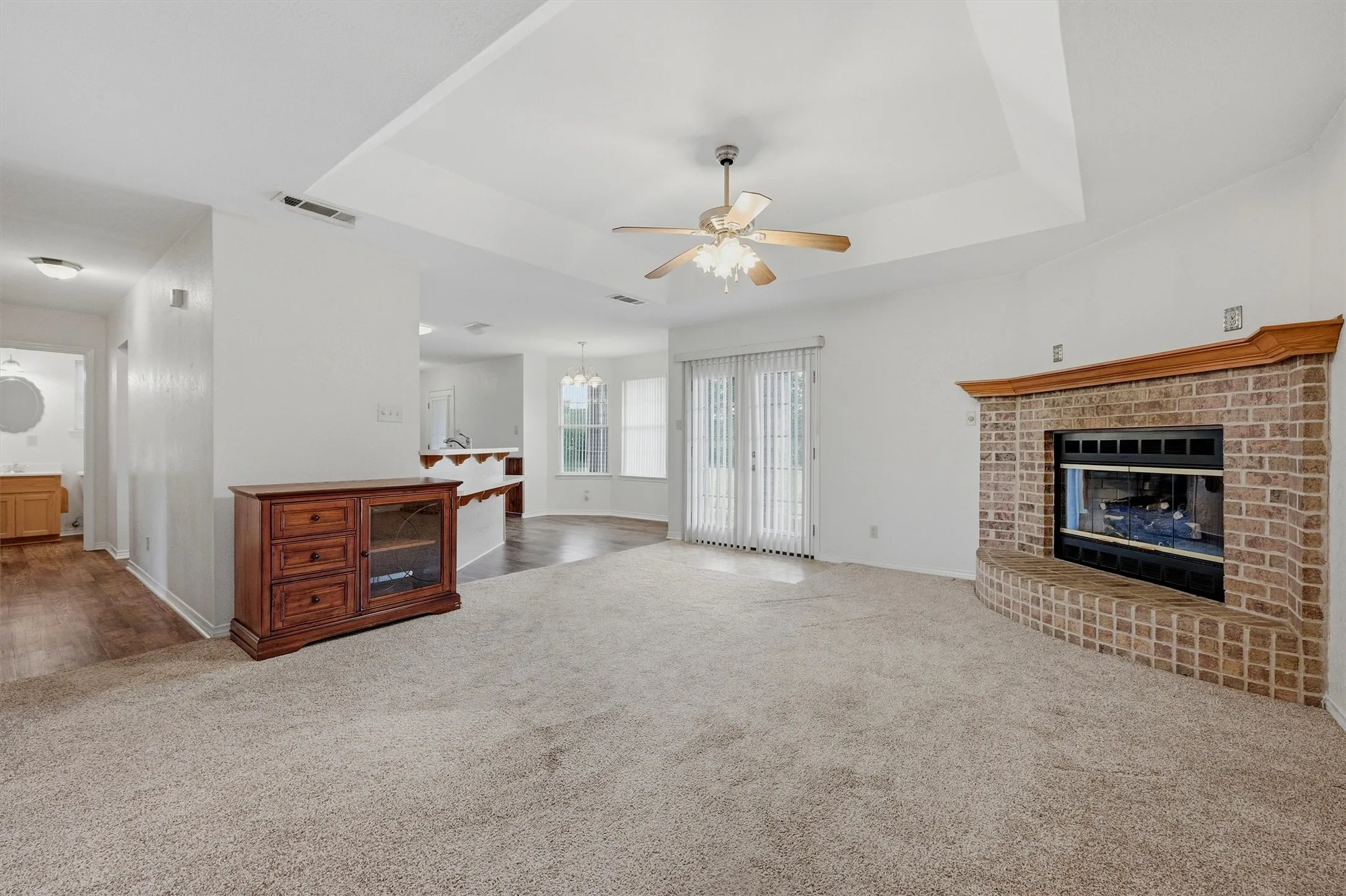 Living area featuring a brick fireplace with wood mantel, tray ceiling, ceiling fan, and carpeted flooring