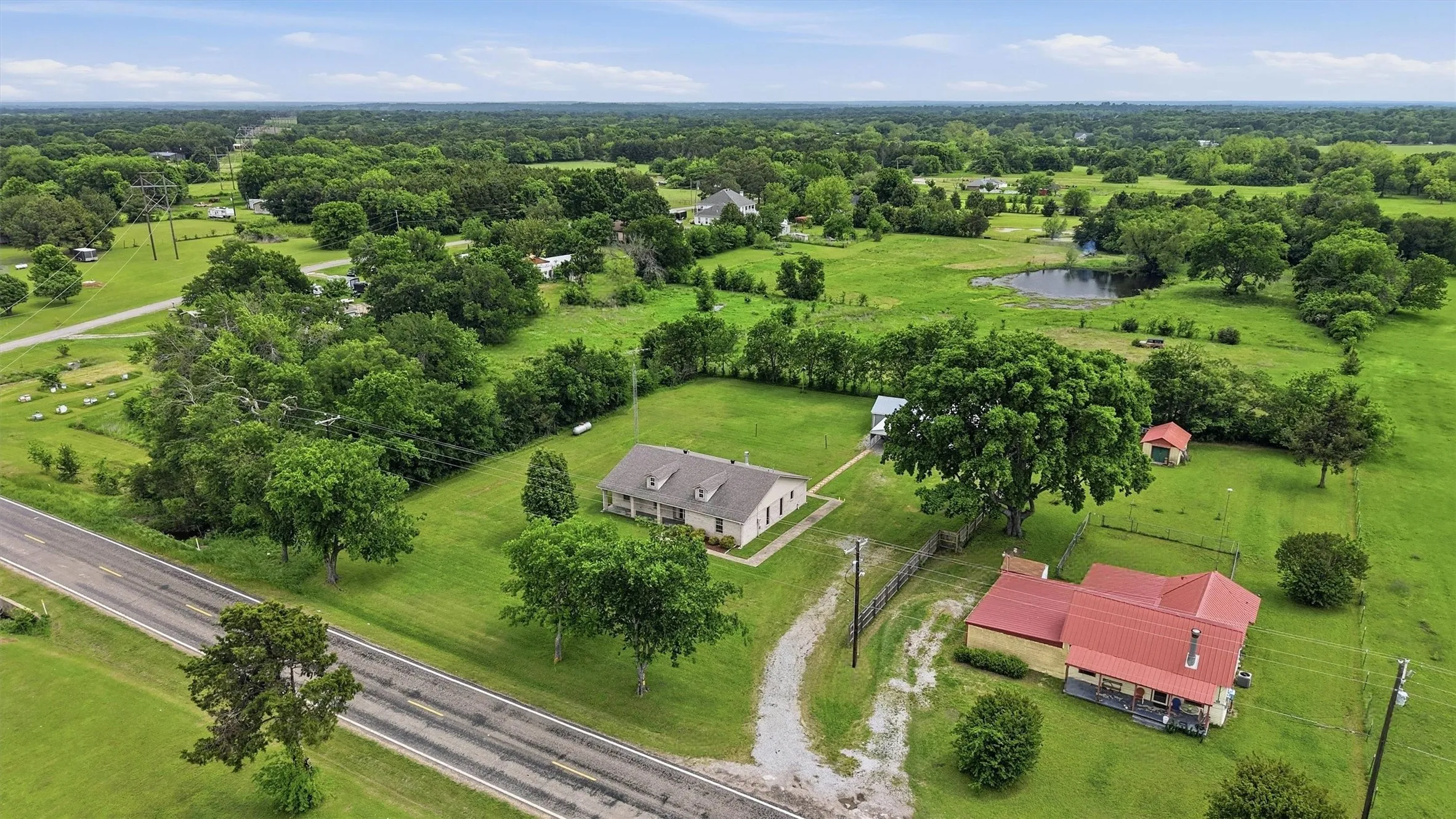 Expansive green acreage featuring two distinct residential structures, a private pond, and mature trees