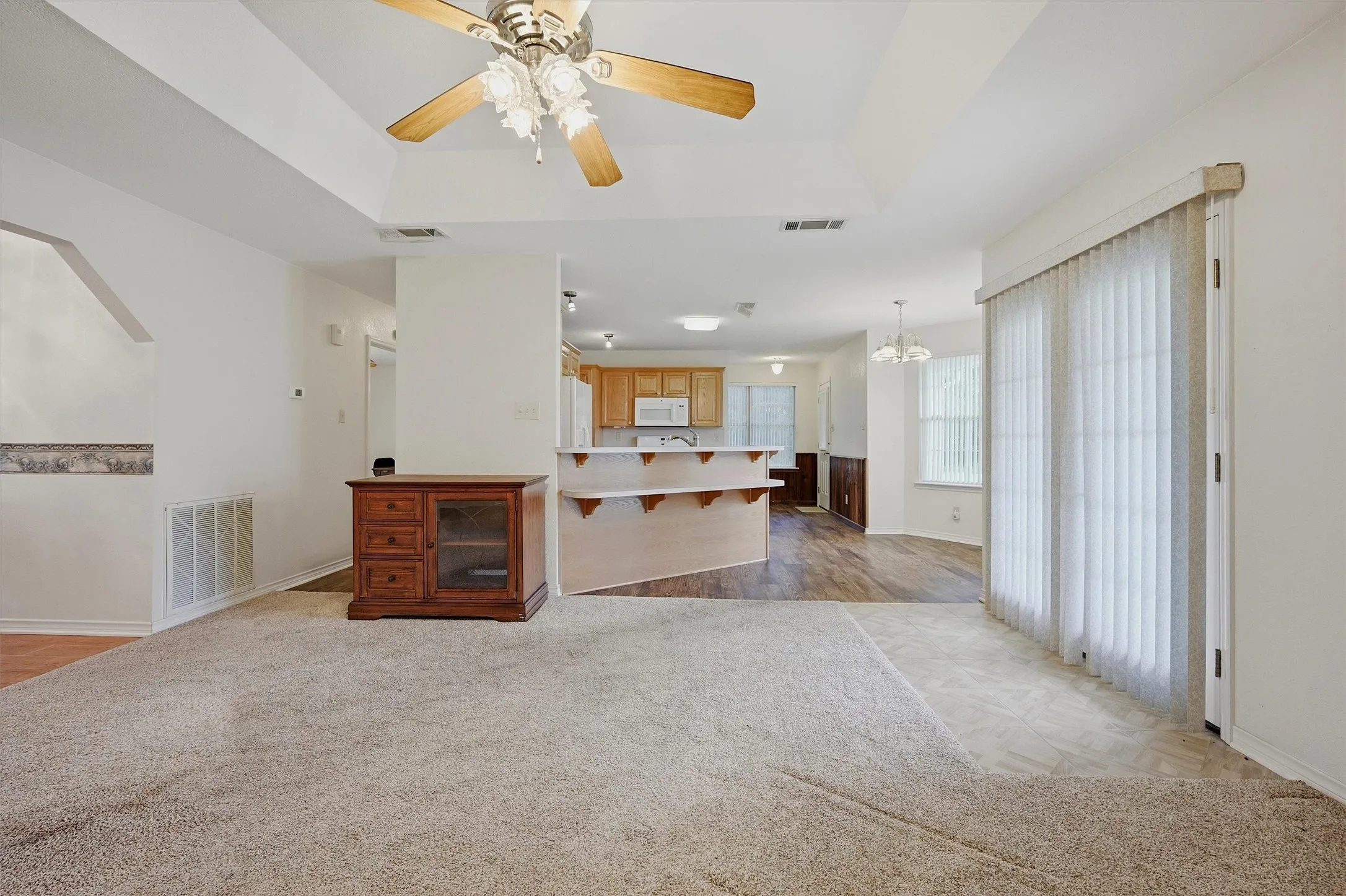 Living area featuring a tray ceiling with a ceiling fan, carpet flooring, and vertical blinds on the sliding glass door
