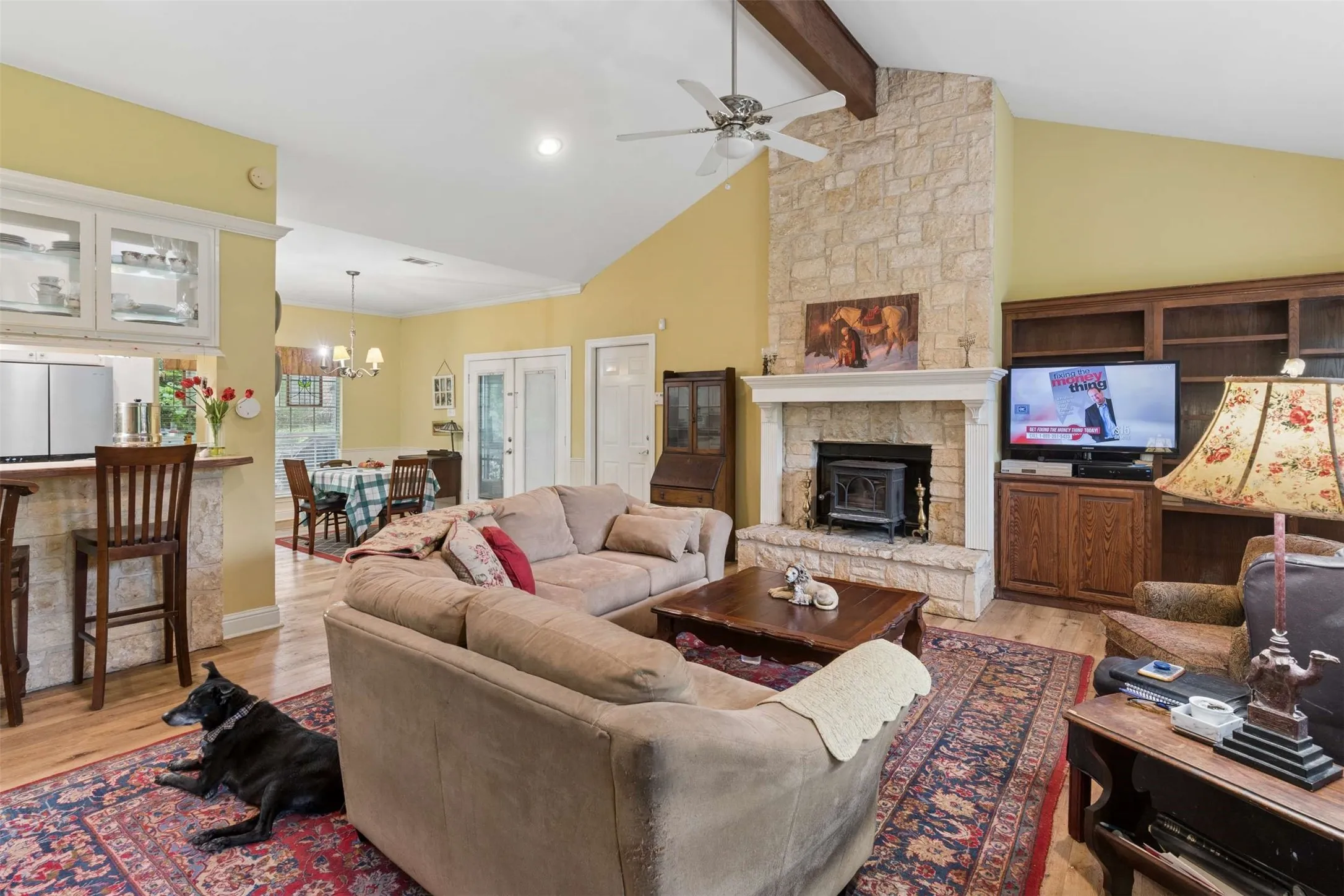 Living area featuring vaulted ceilings with exposed wood beams, a stone fireplace with a wood-burning insert, and wood-finish flooring