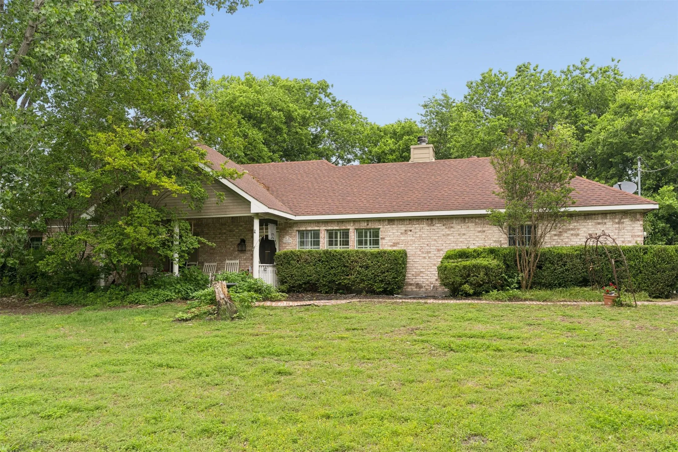 Traditional brick exterior with a brown shingle roof, featuring a covered front porch and mature landscaping