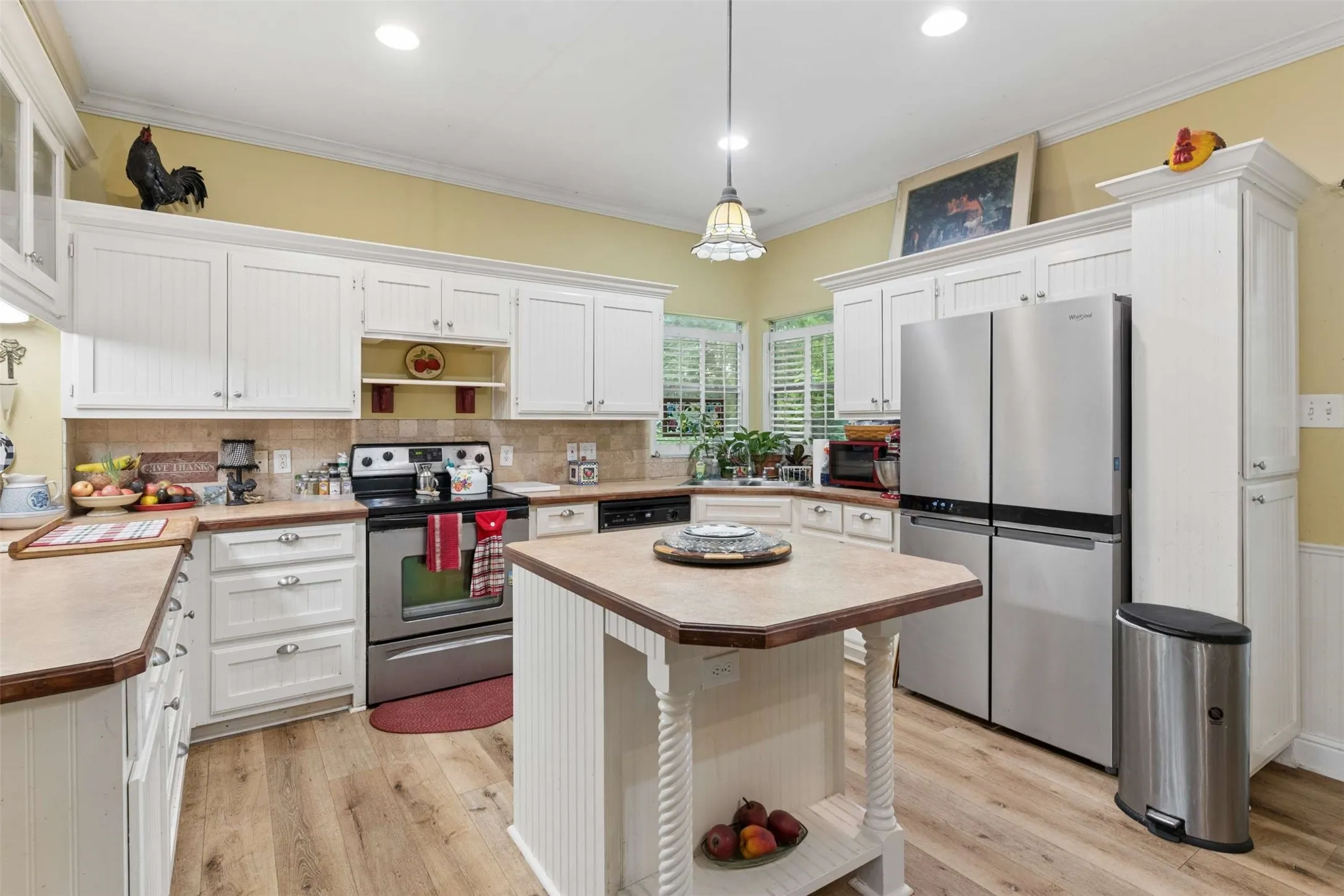Kitchen featuring wood-finish flooring, white cabinetry, stainless steel appliances, a center island, and a tile backsplash