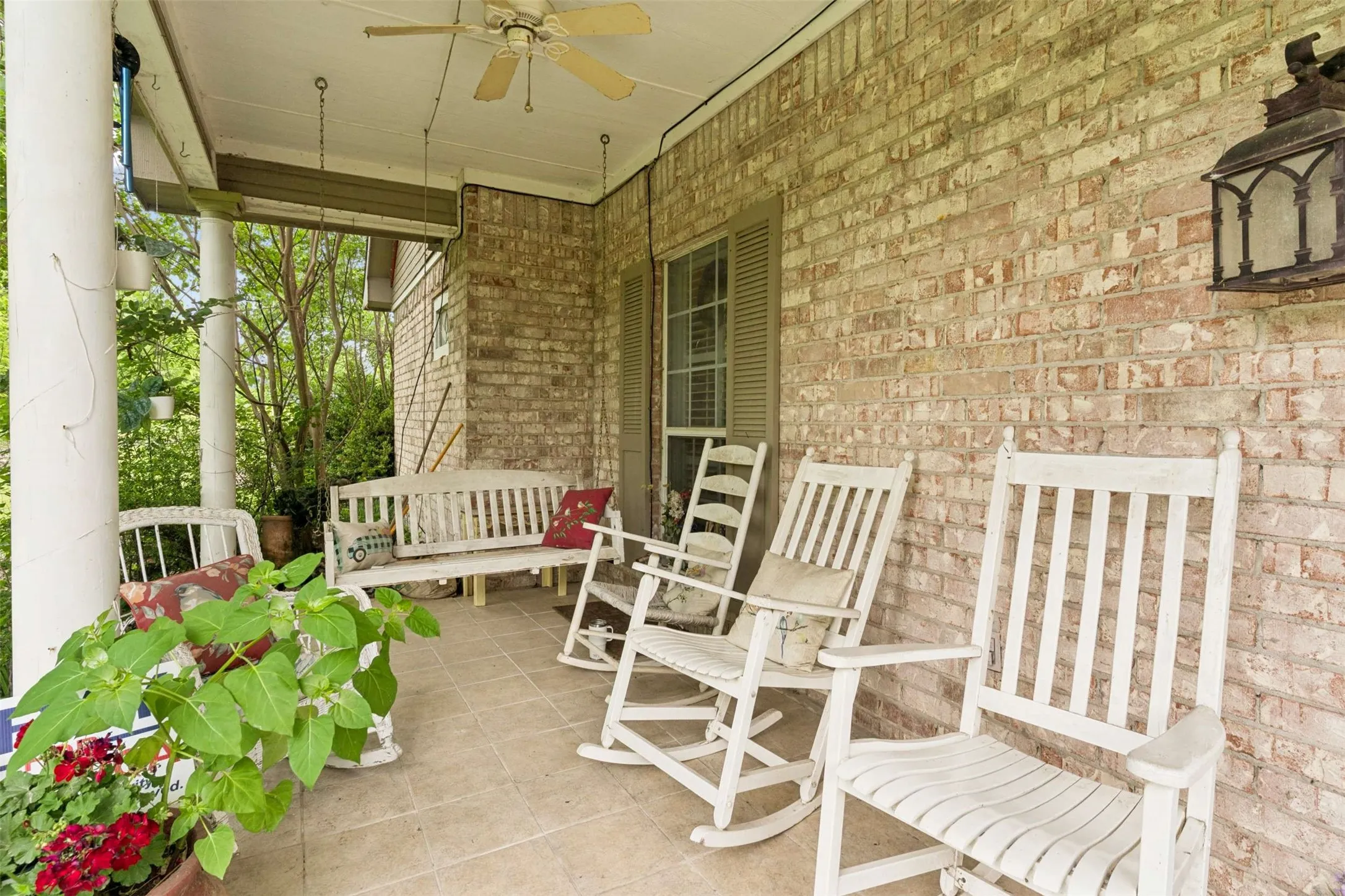 Brick exterior porch featuring a ceiling fan, suspended lantern-style light fixture, and tile flooring