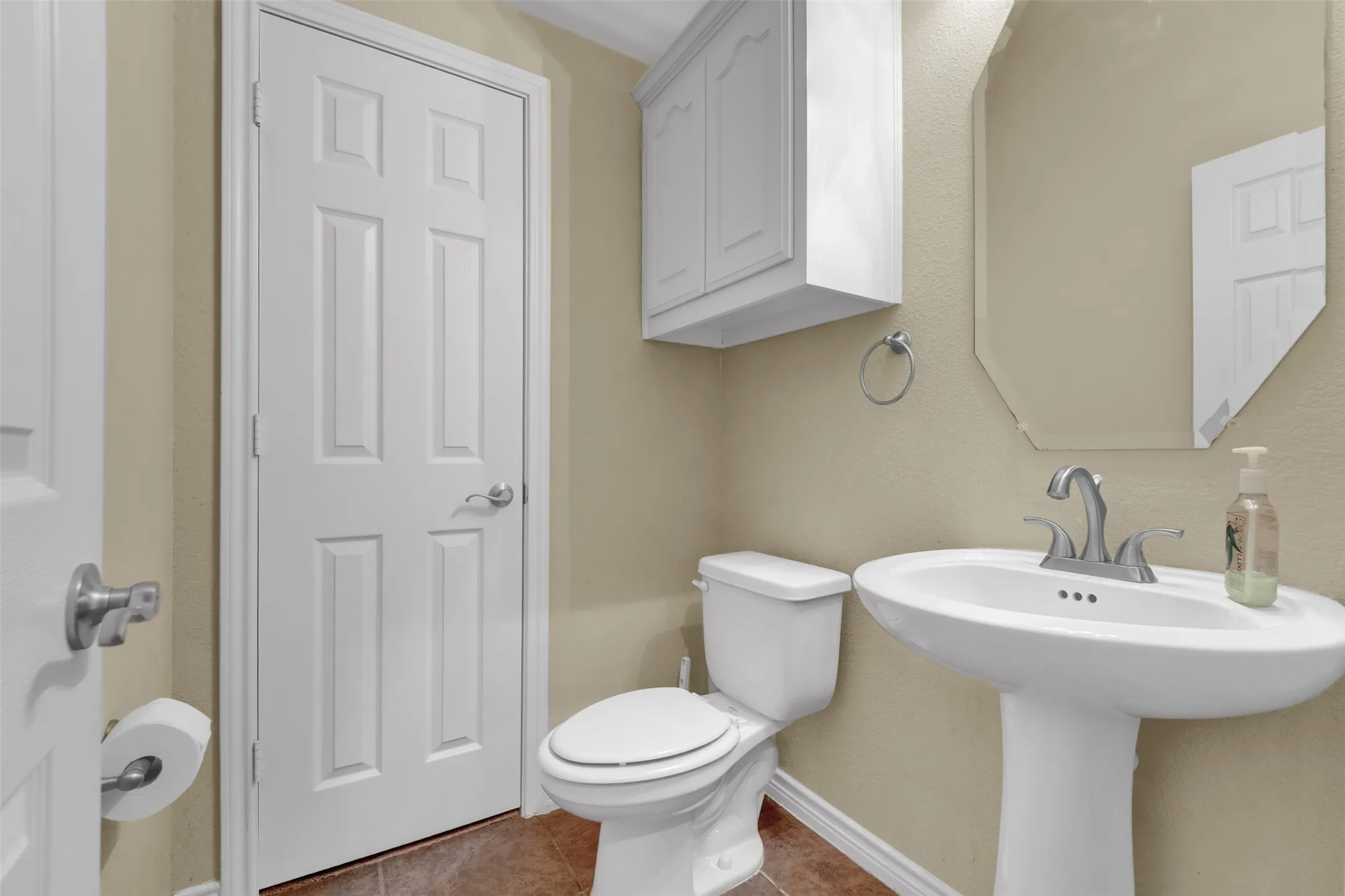 Pedestal sink with chrome faucet, octagonal mirror, and wall-mounted storage cabinet