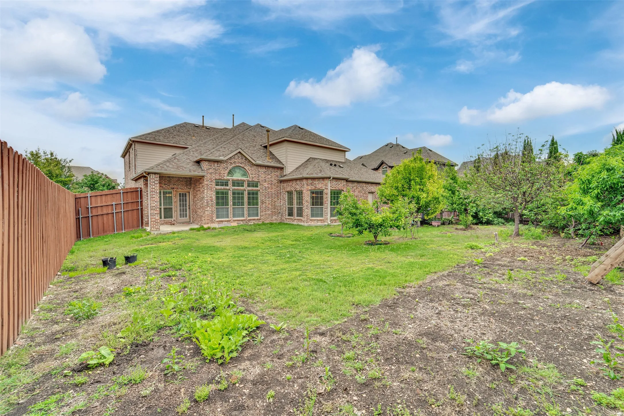 Spacious backyard featuring a wood privacy fence, mature trees, and a brick exterior with multiple windows