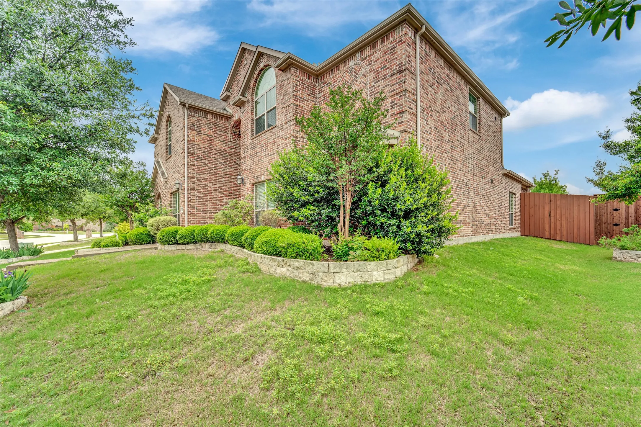 Two-story brick exterior with arched window accents, stone retaining walls, established landscaping, and a privacy fence