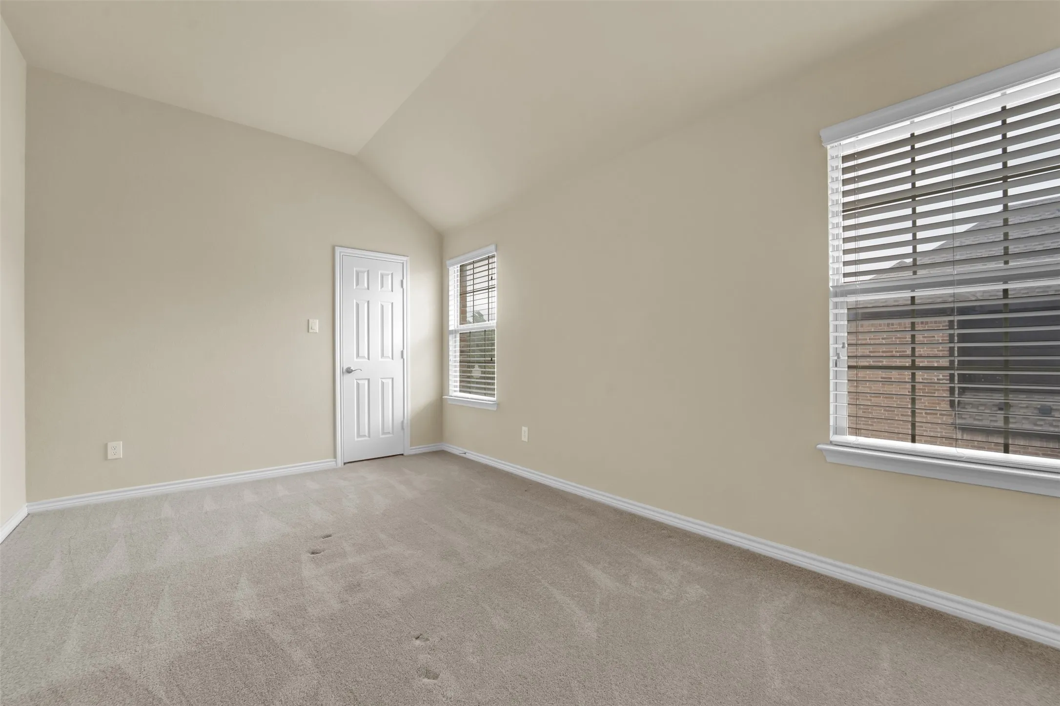 Carpeted room with a vaulted ceiling, multiple windows with blinds, and a white paneled door