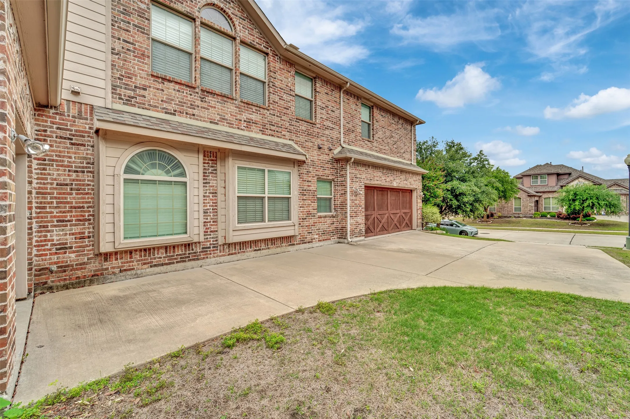 Brick exterior featuring an arched transom window, a two-car garage with cross-brace detailing, and a concrete driveway