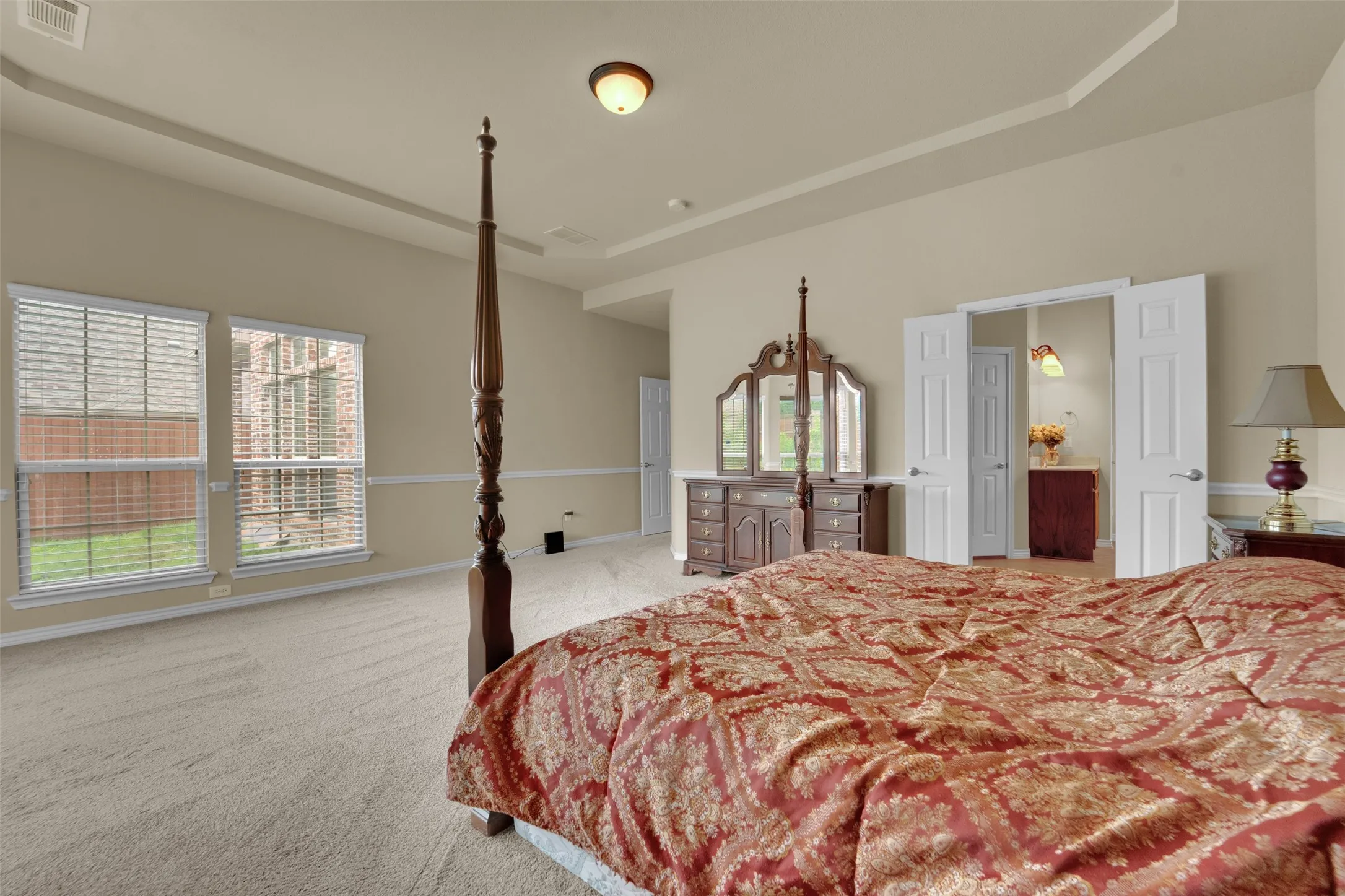 Spacious bedroom featuring neutral wall tones, tray ceiling, and carpeted flooring