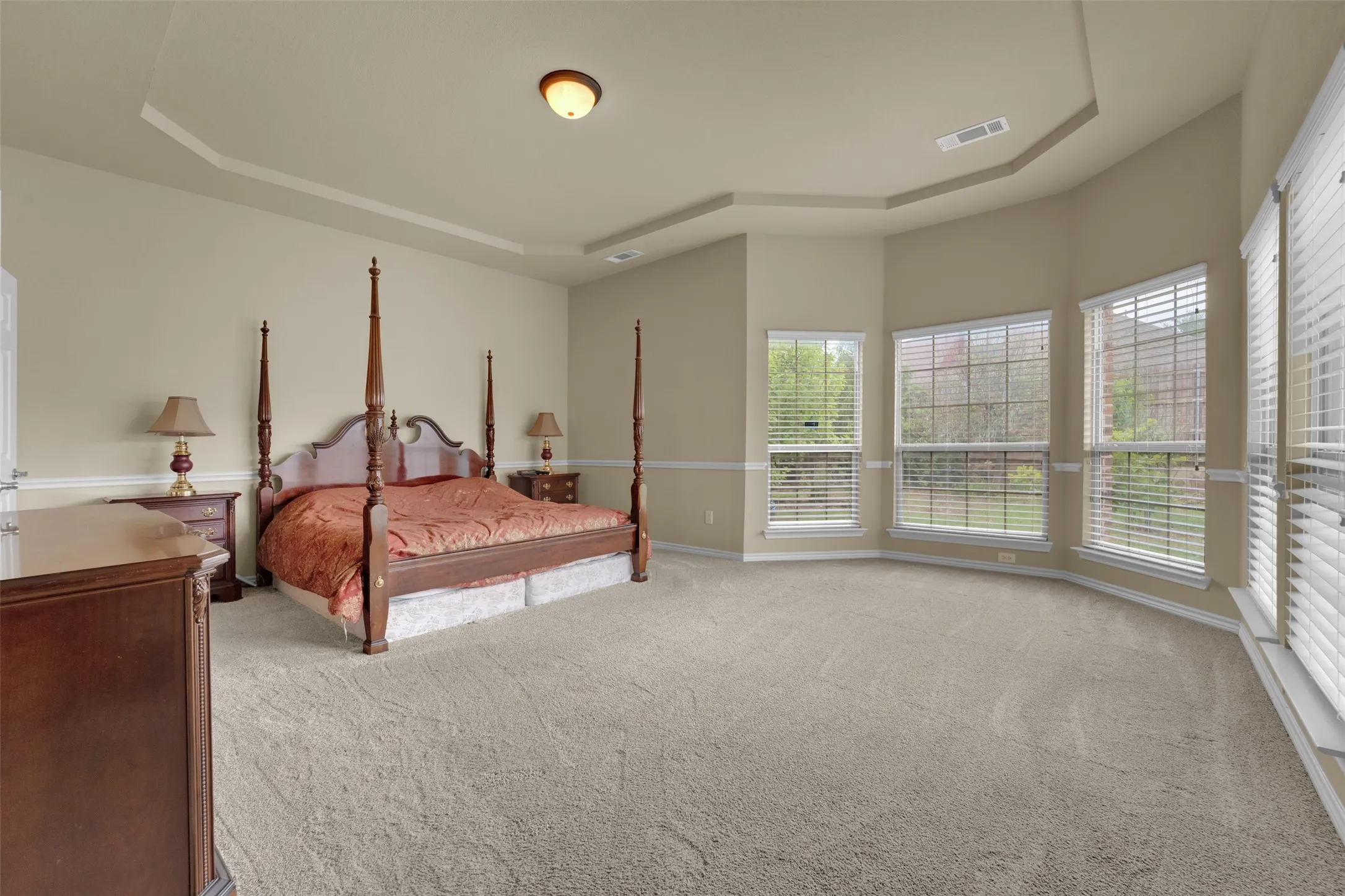 Carpeted room featuring a tray ceiling and multiple windows with blinds