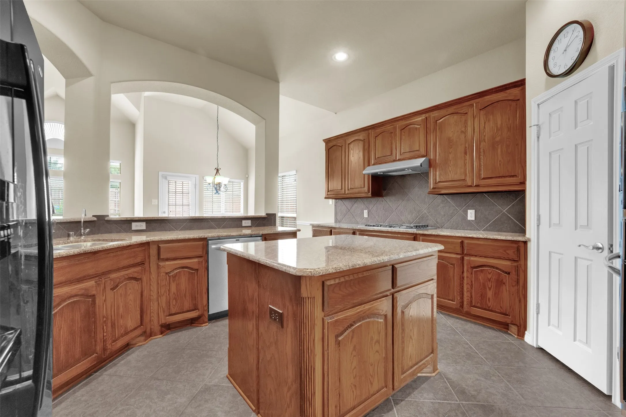 Kitchen featuring a central island, wood cabinetry, granite countertops, tile flooring, and a tile backsplash