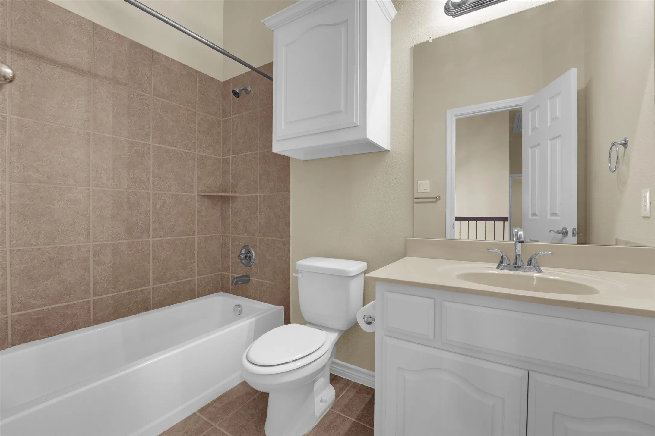 Bathroom featuring a white vanity with an integrated sink, a large mirror, a white toilet, and a bathtub with a tiled surround