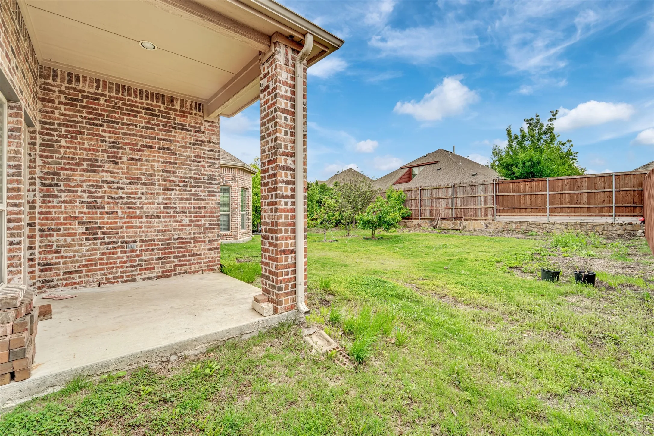 Covered concrete patio with brick support columns and a spacious grass yard, enclosed by a wood fence