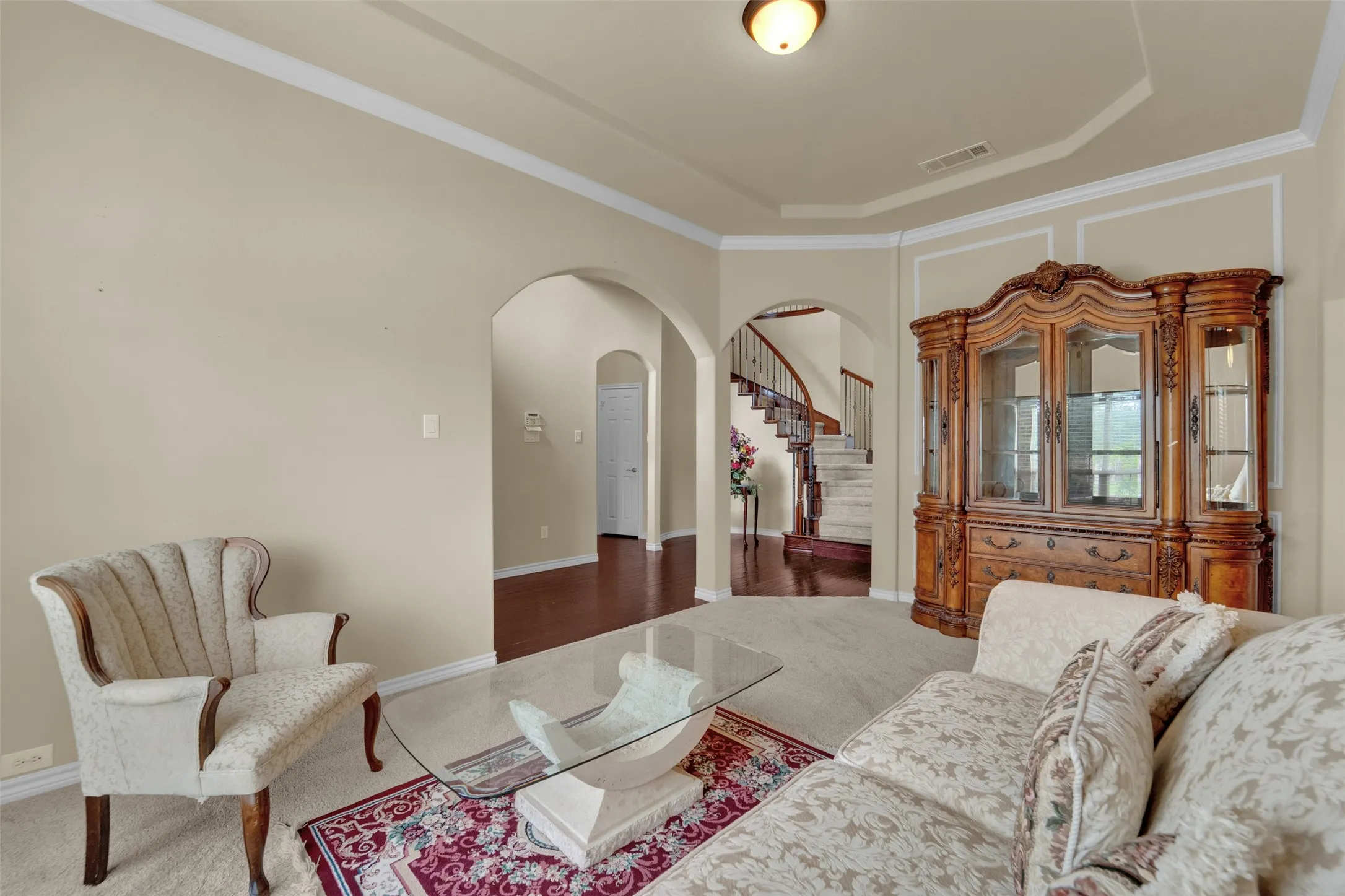 Living area featuring neutral wall tones, arched doorways, a tray ceiling, and crown molding