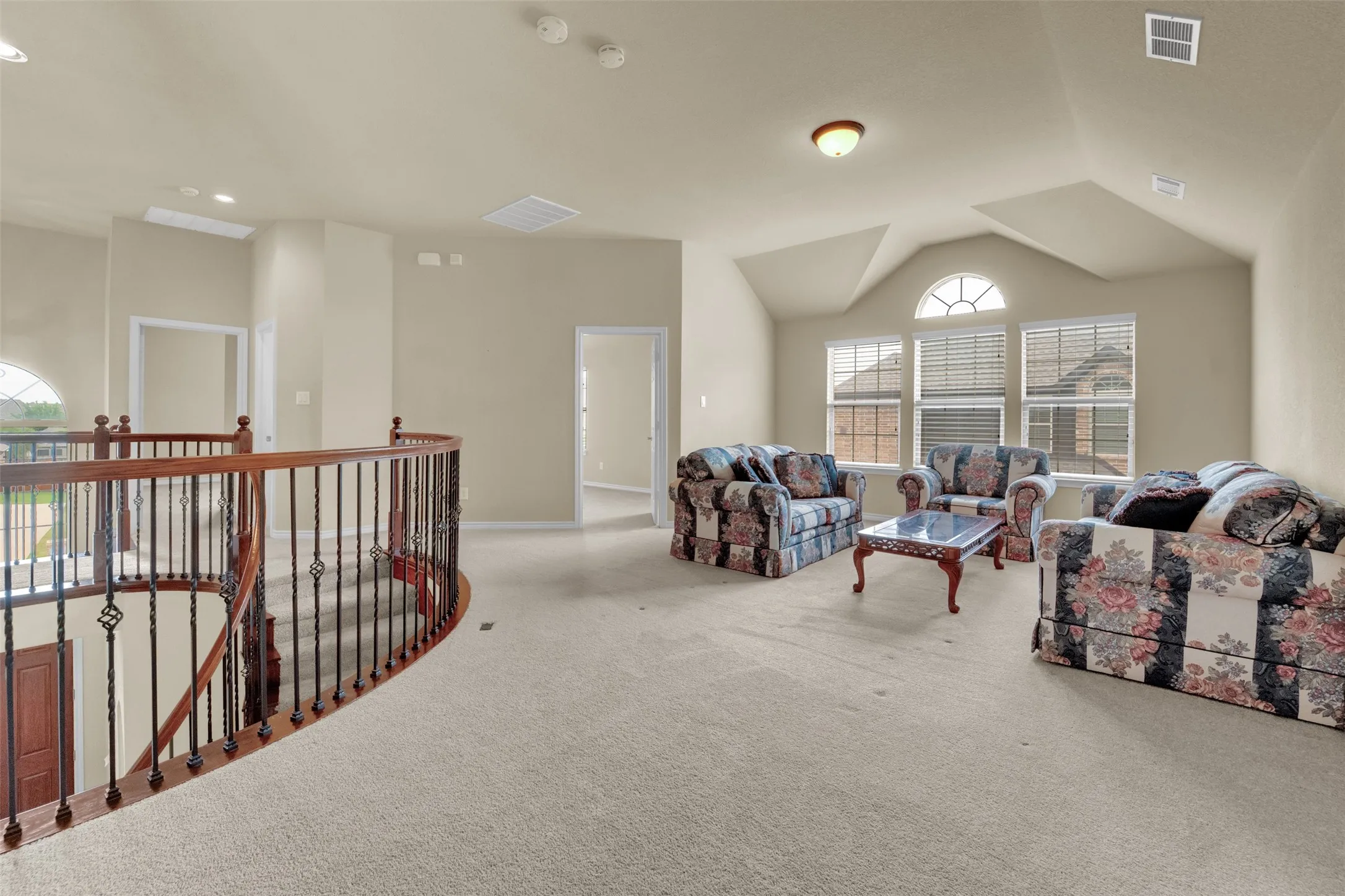 Spacious upper-level area featuring light-colored carpet flooring and multiple windows with blinds
