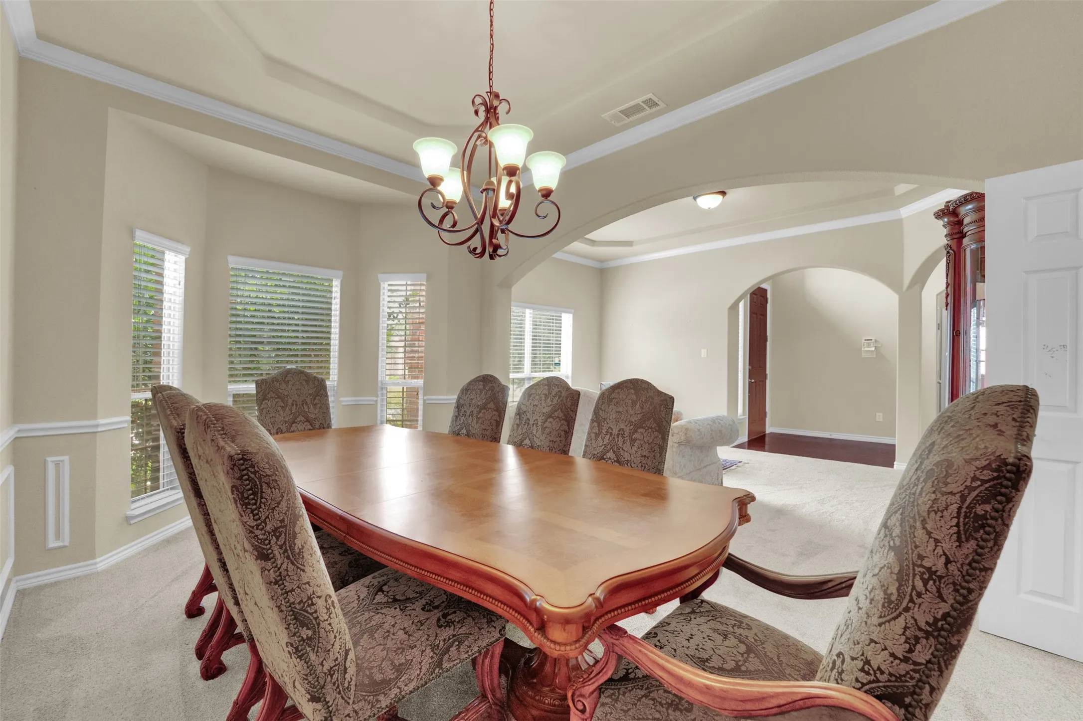 Elegant dining area featuring a tray ceiling with crown molding, a decorative chandelier, and wainscoting