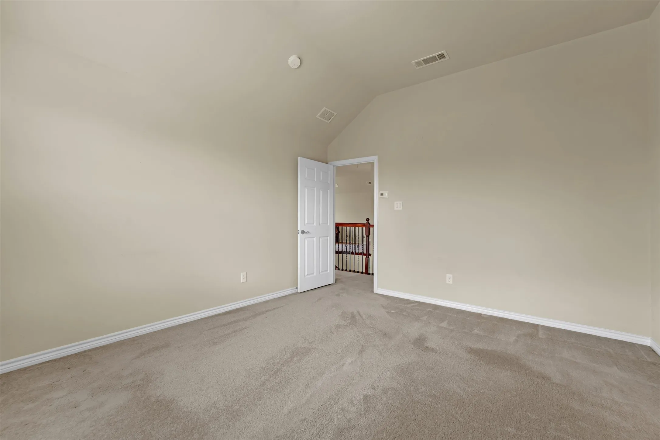 Carpeted room featuring a vaulted ceiling and neutral wall tones