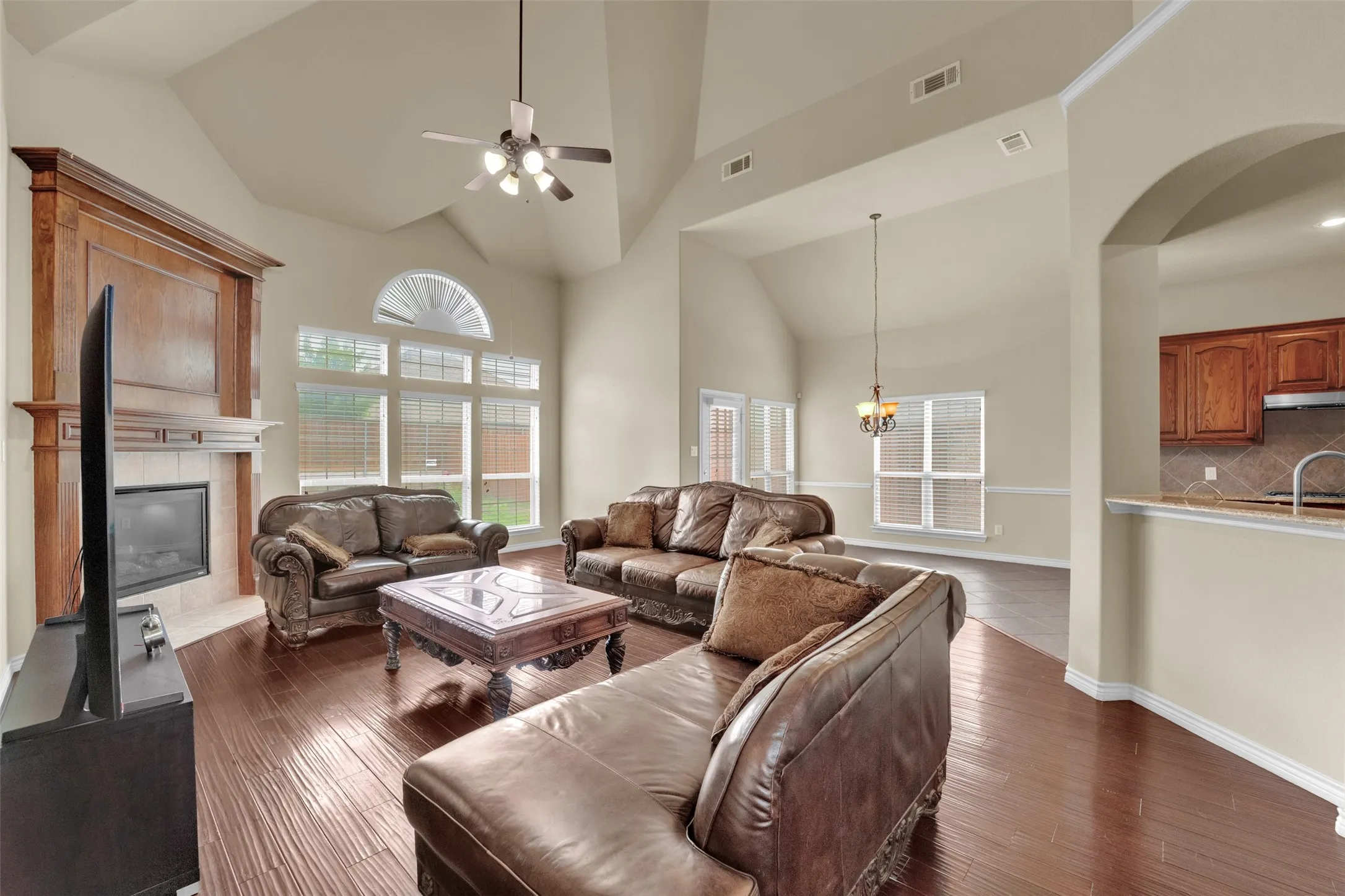 Spacious living area featuring high vaulted ceilings, wood-finish flooring, and a fireplace with a wood mantel