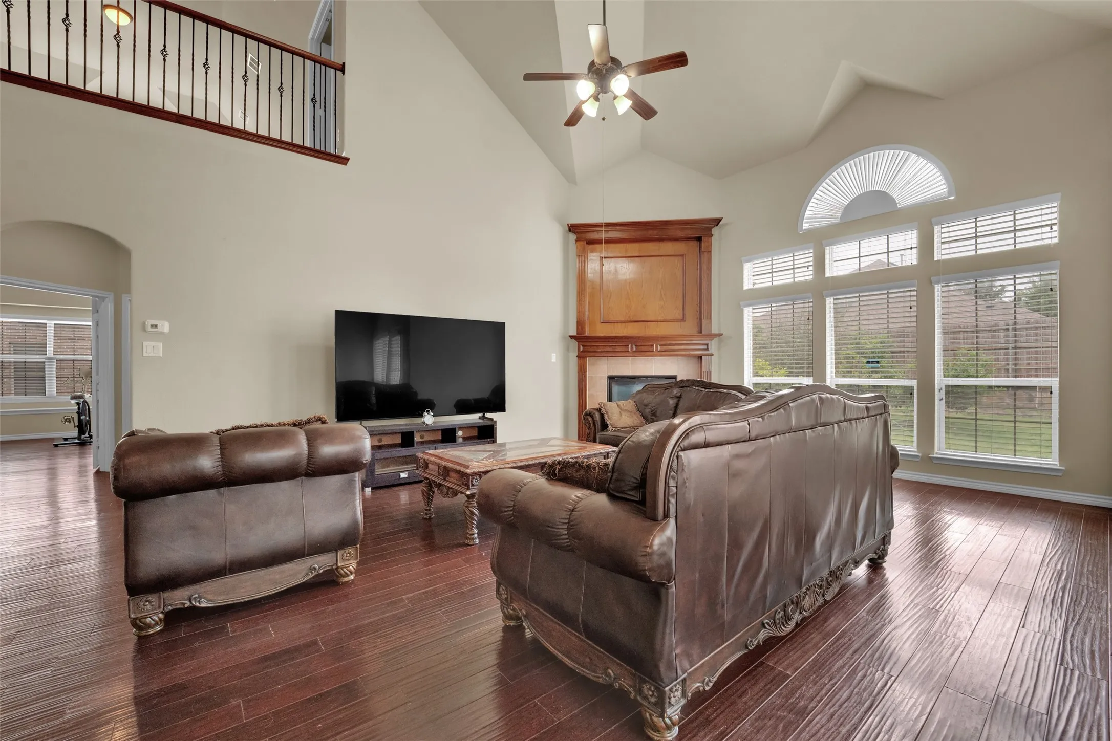 Spacious living area featuring high vaulted ceilings, rich wood-finish flooring, and a corner fireplace with a detailed wood mantle