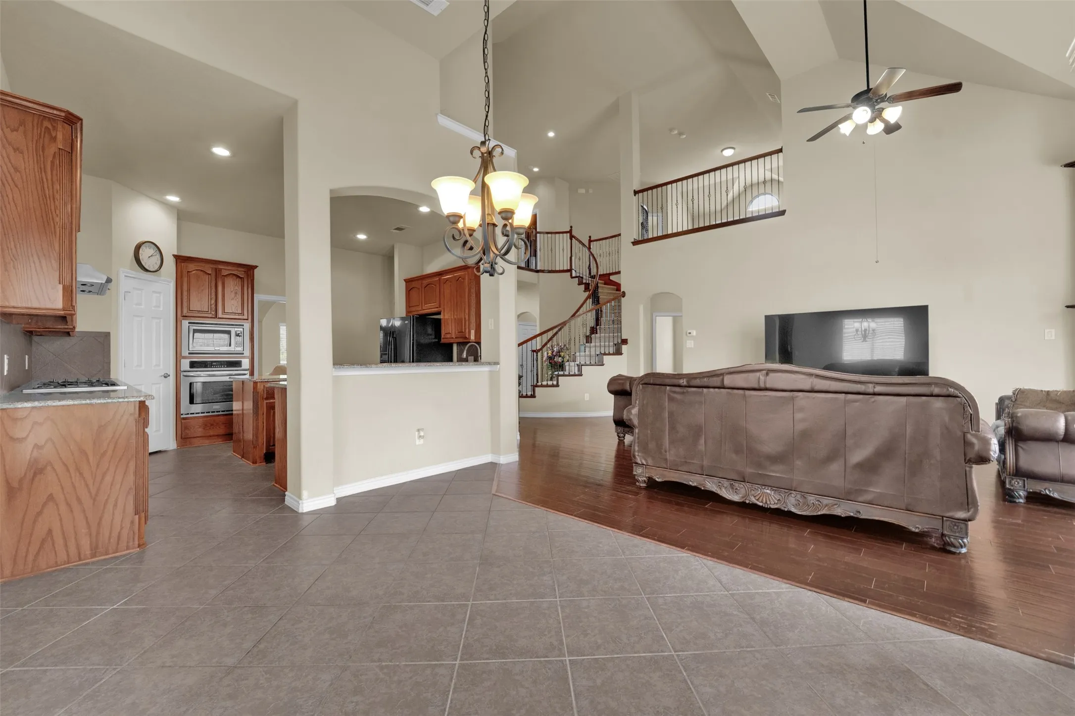 Open-concept living area featuring a vaulted ceiling, wood-finish flooring, and a grand spiral staircase with wrought iron balusters
