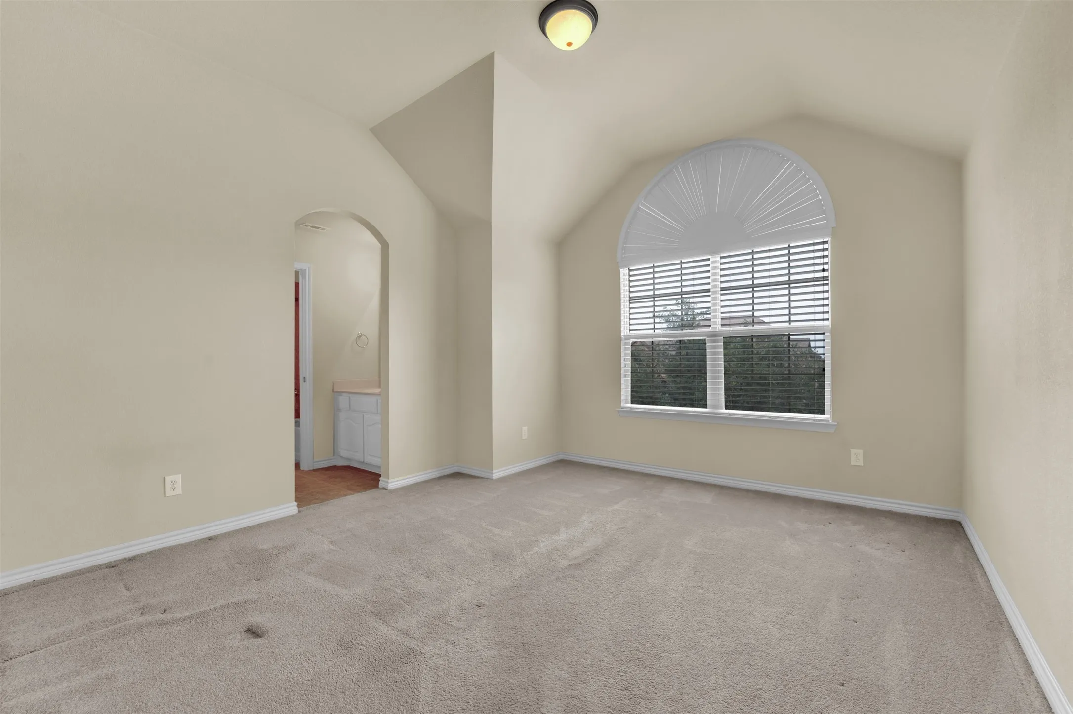 Vaulted ceiling room with an arched window featuring horizontal blinds and a fan-shaped arch window covering