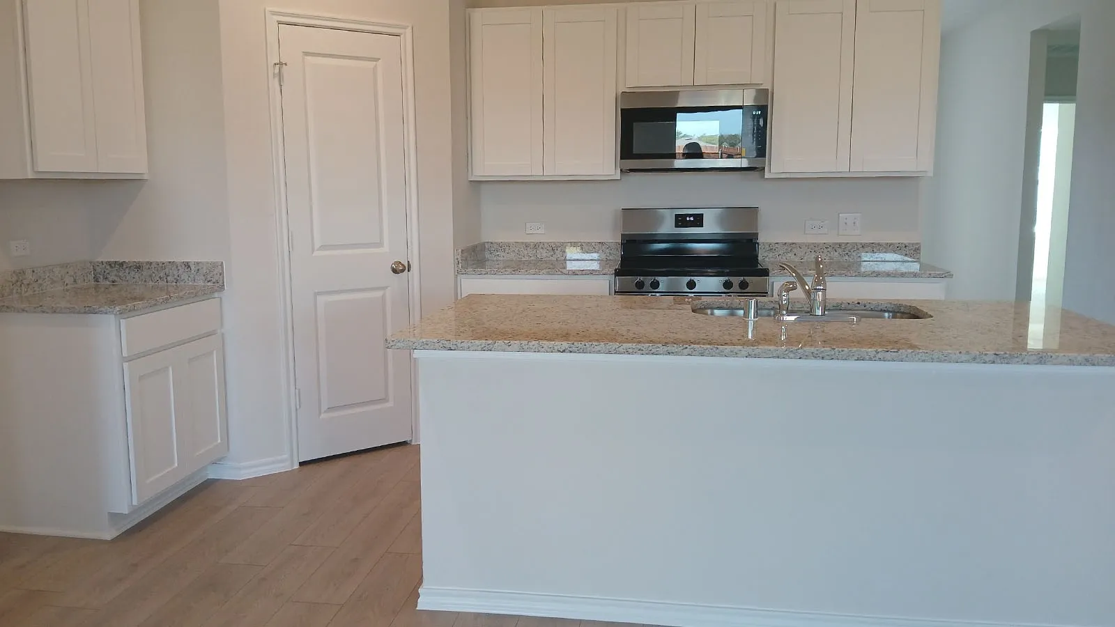 Kitchen featuring light wood-finish flooring, white cabinetry, speckled countertops, stainless steel appliances, and a built-in sink