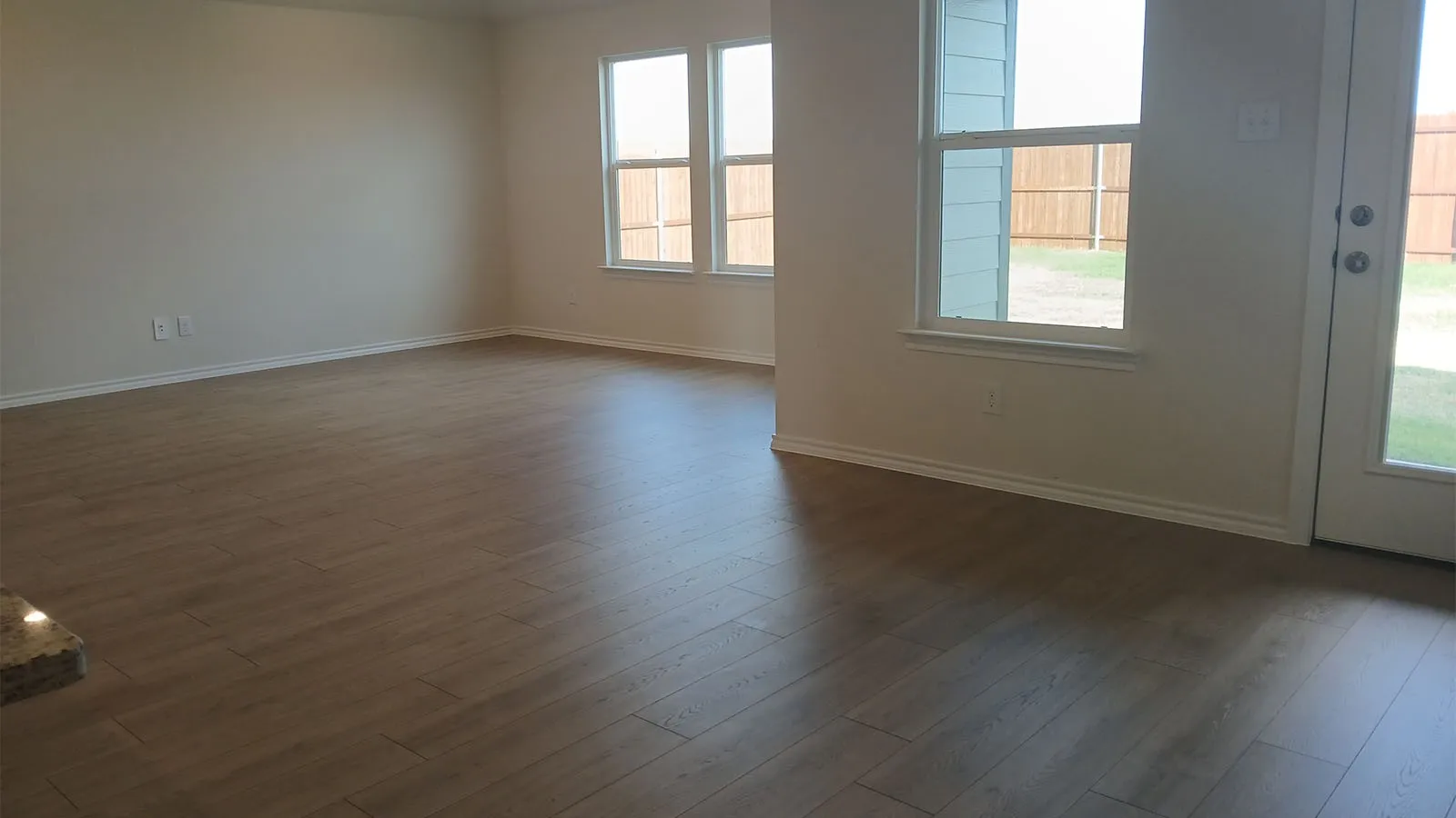 Spacious room with wood-finish flooring, multiple windows, and a glass-paneled door