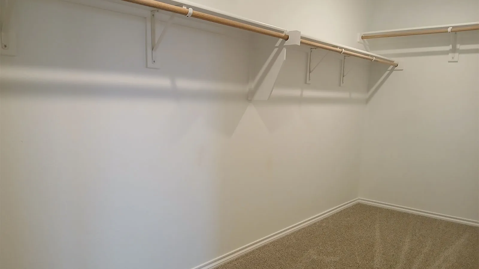 Carpeted closet space featuring white walls and multiple wooden hanging rods with white supports
