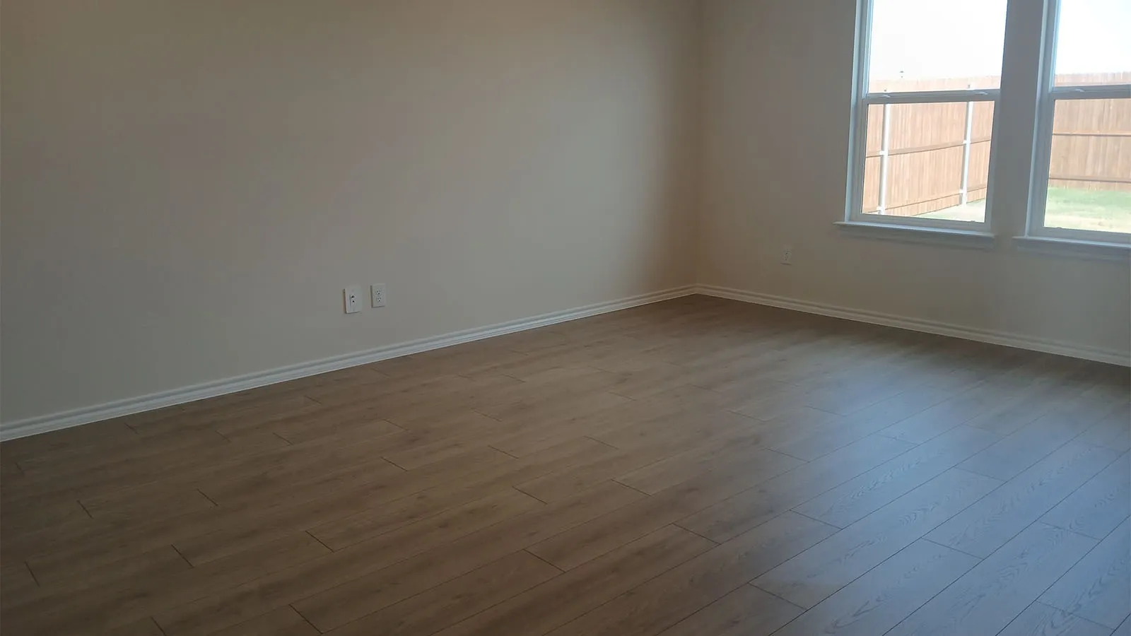 Wood-finish flooring throughout, light neutral wall paint, and two windows with white trim