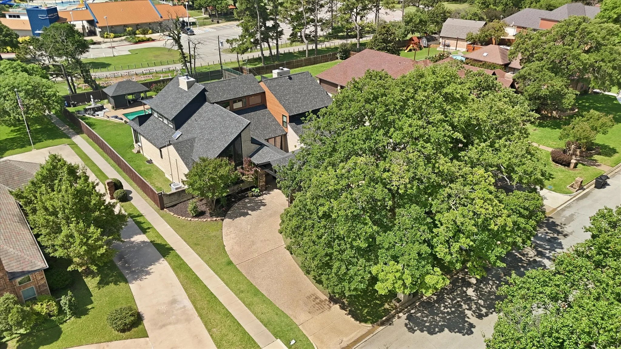 Aerial perspective of this unique home situated in Colleyville. Mature tree, circular driveway, lots of windows and a big backyard with pool and sports court.