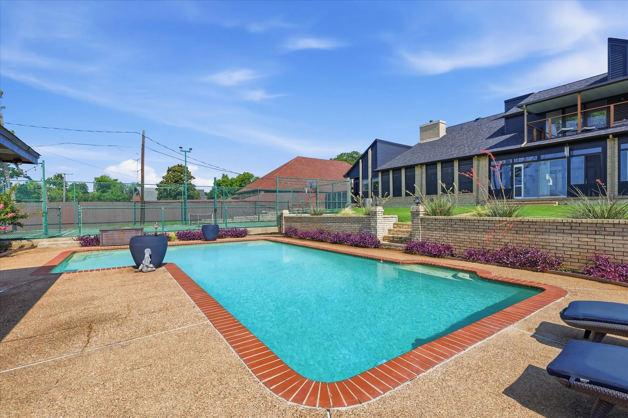 Spacious outdoor living area featuring a large pool, an adjacent sports court, and a multi-level patio with stone steps