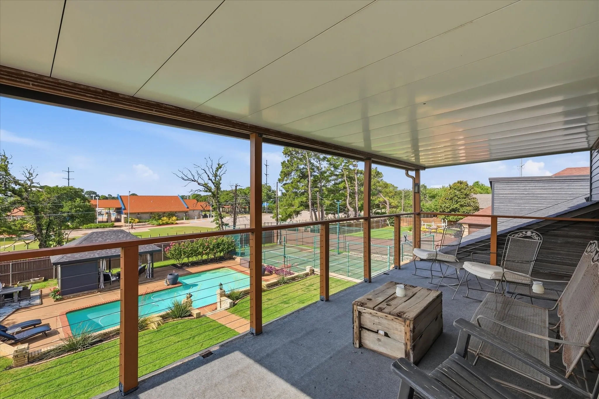 Covered outdoor balcony with recently installed metal roof, ample space and views of the large backyard featuring a sports court, large pool, grass, and poolside cabana.