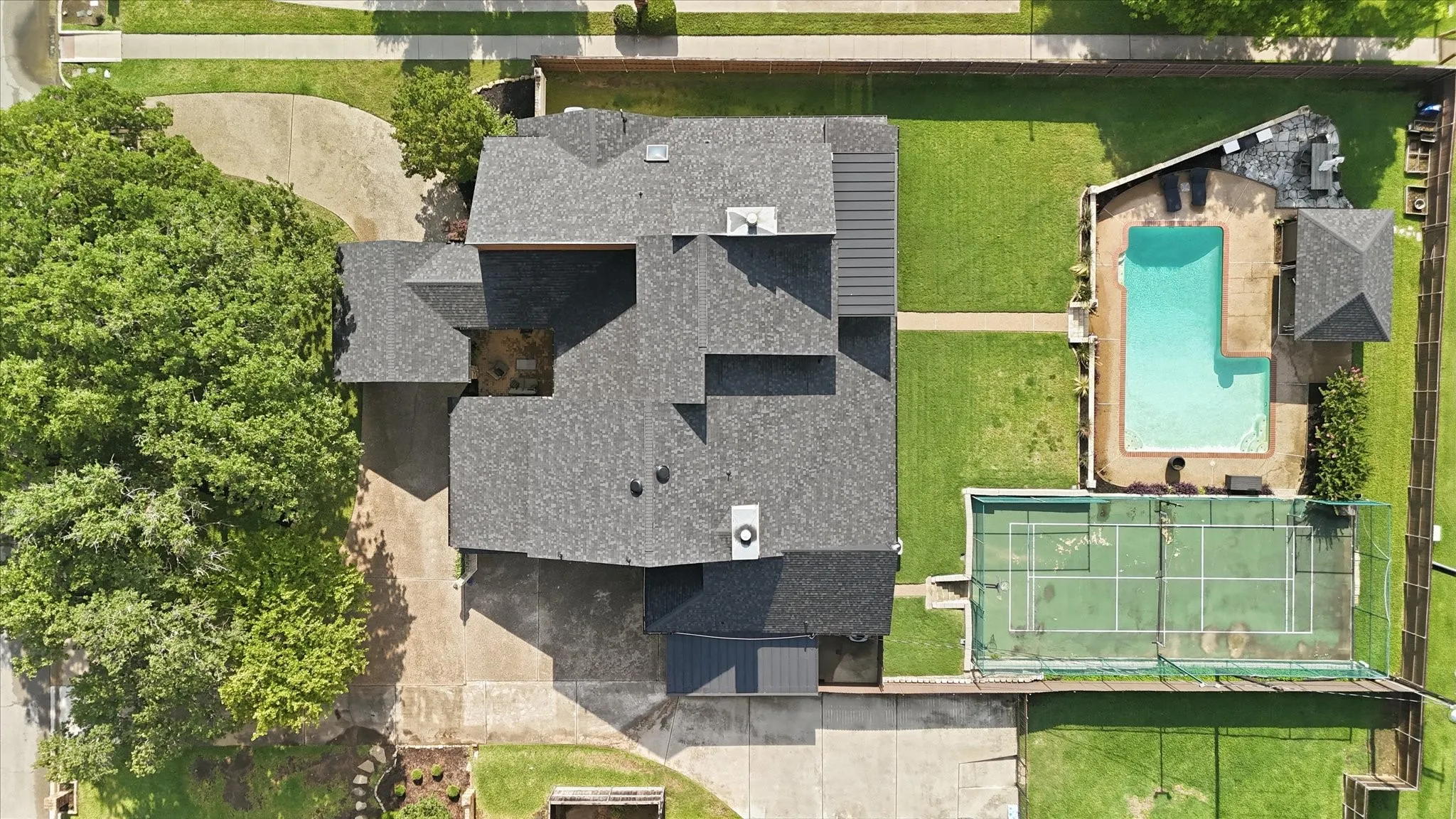 Expansive almost-half-acre property featuring a multi-level roofline, a large in-ground pool with spacious pool deck, a dedicated sports court, and mature landscaping